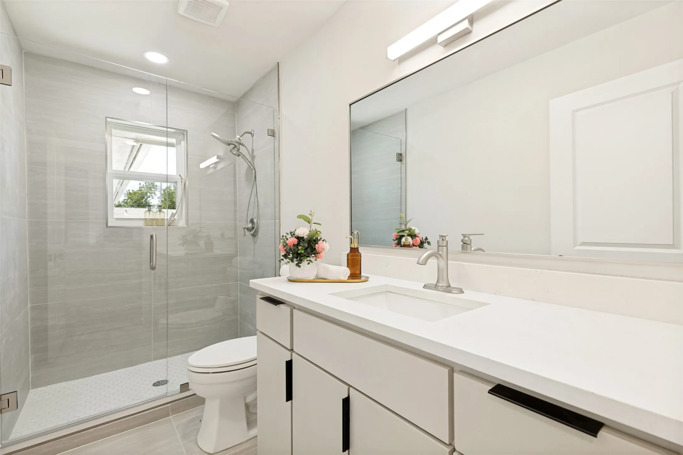 Glass-enclosed shower with a rainfall showerhead, large format wall tile, and mosaic tile flooring