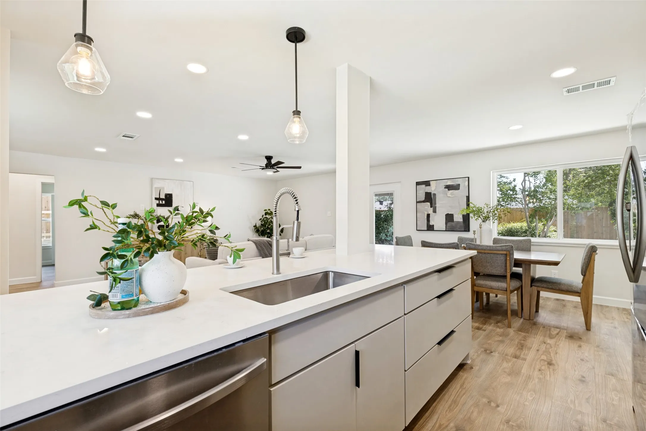 Kitchen island with integrated sink, stainless steel dishwasher, modern pendant lighting, wood-finish flooring, and recessed ceiling lights