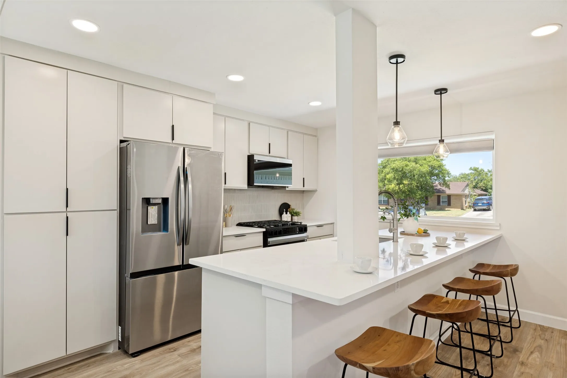 Kitchen featuring white cabinetry, stainless steel appliances, a white countertop island with seating, pendant lighting, and wood-finish flooring