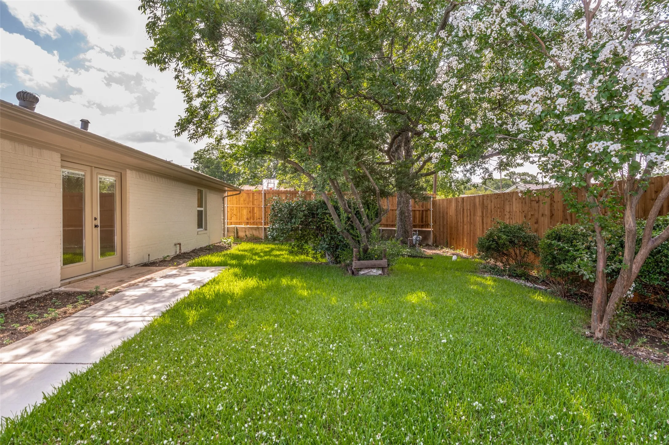 Expansive backyard featuring a manicured lawn, established trees, and a wooden privacy fence