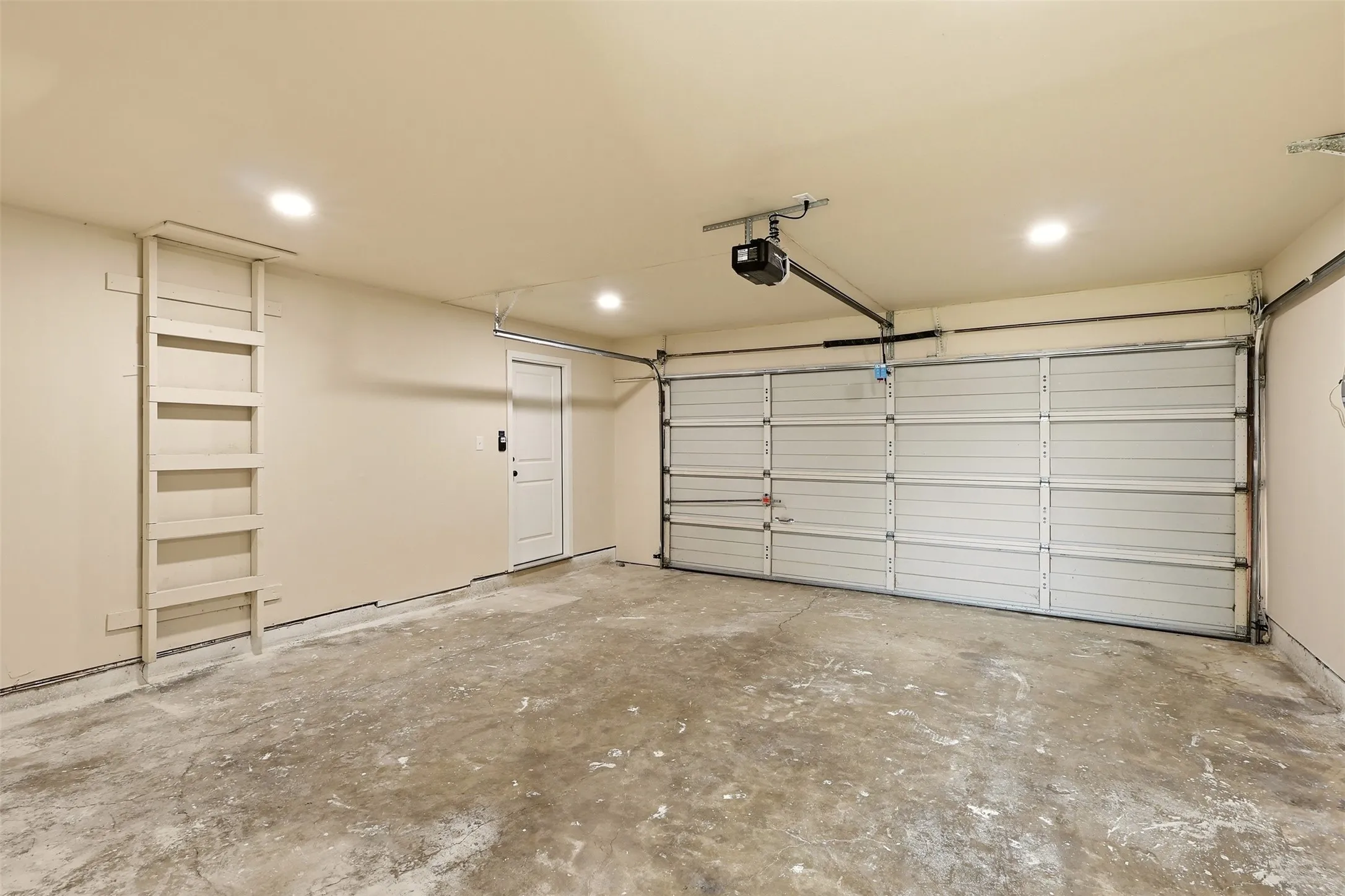 Garage space featuring an automatic overhead door, built-in shelving, concrete flooring, and recessed lighting