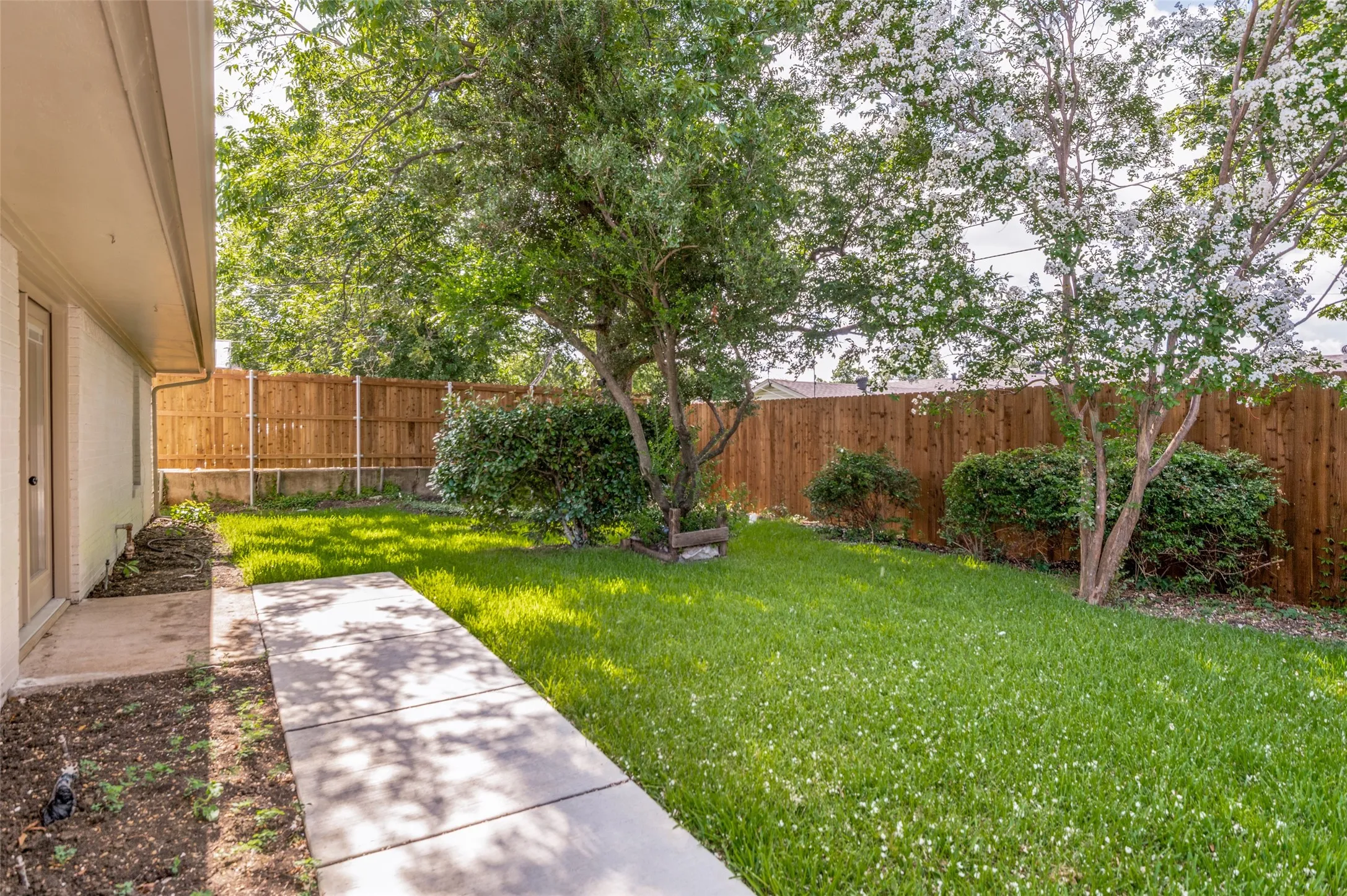 Expansive green lawn with mature trees, shrubbery, and a wood privacy fence
