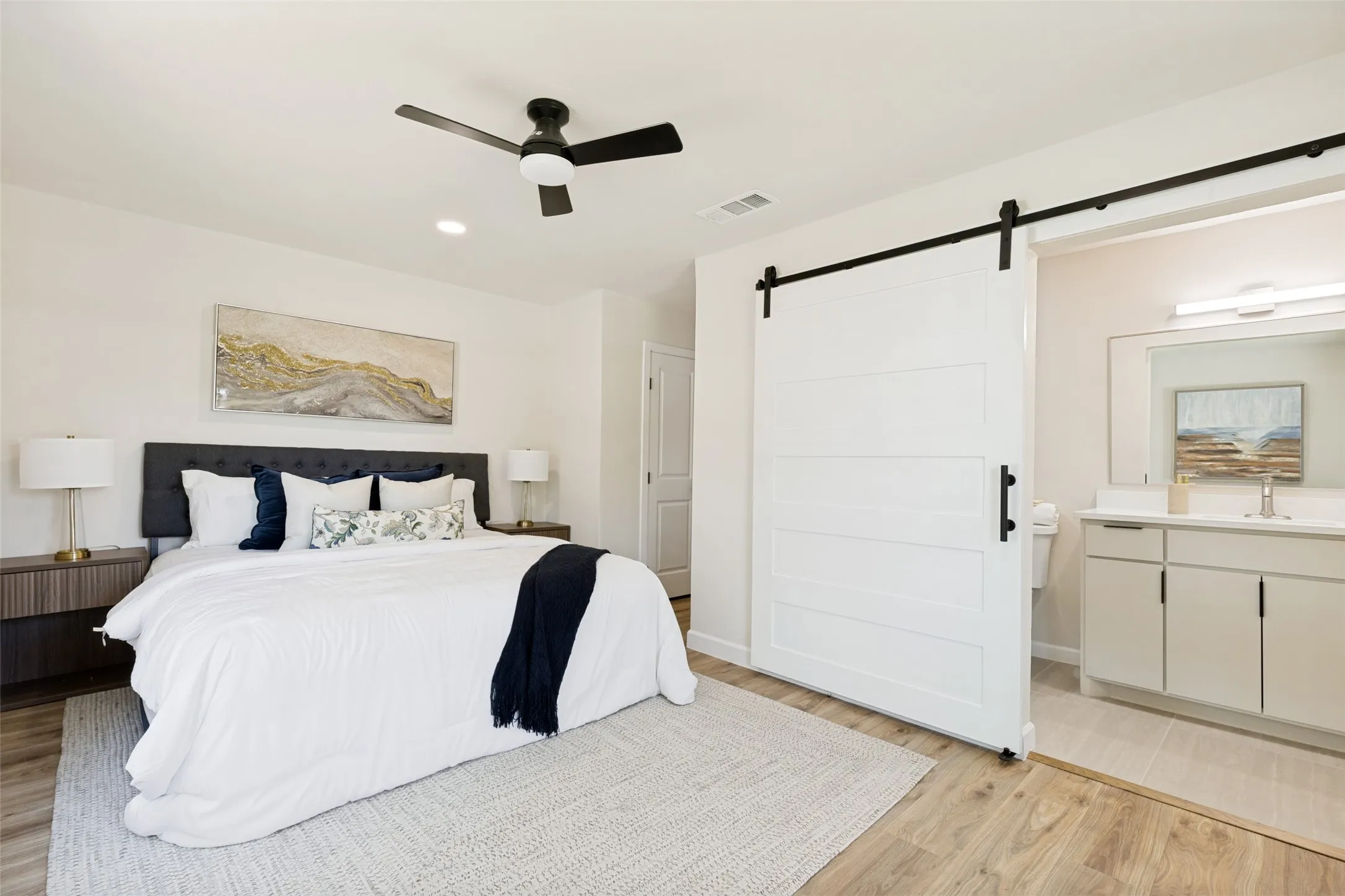 Recessed lighting, ceiling fan, wood-finish flooring, white barn door with black hardware, and bathroom vanity with single sink
