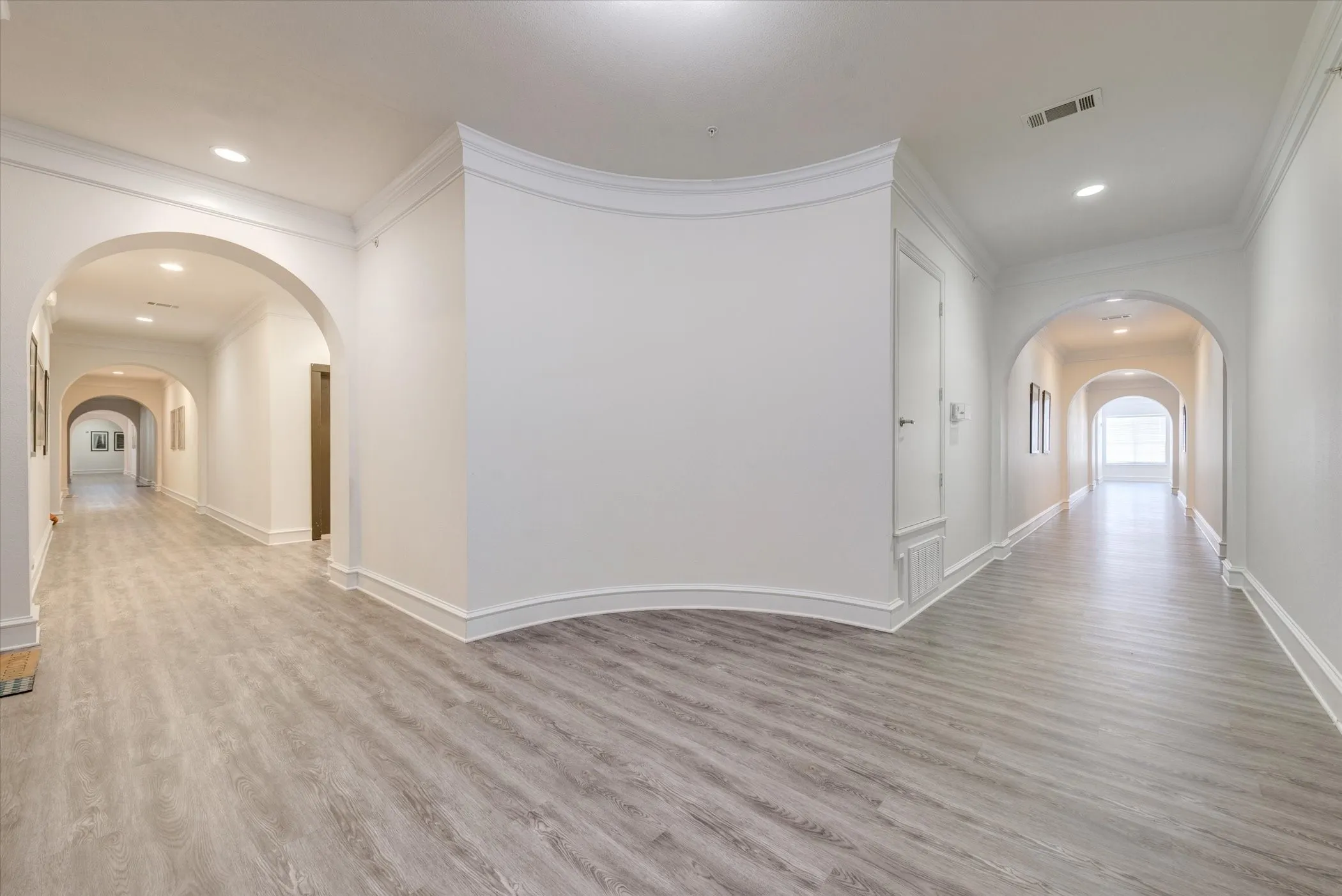 Corridor with arched walkways, ornamental molding, wood finished floors, and recessed lighting