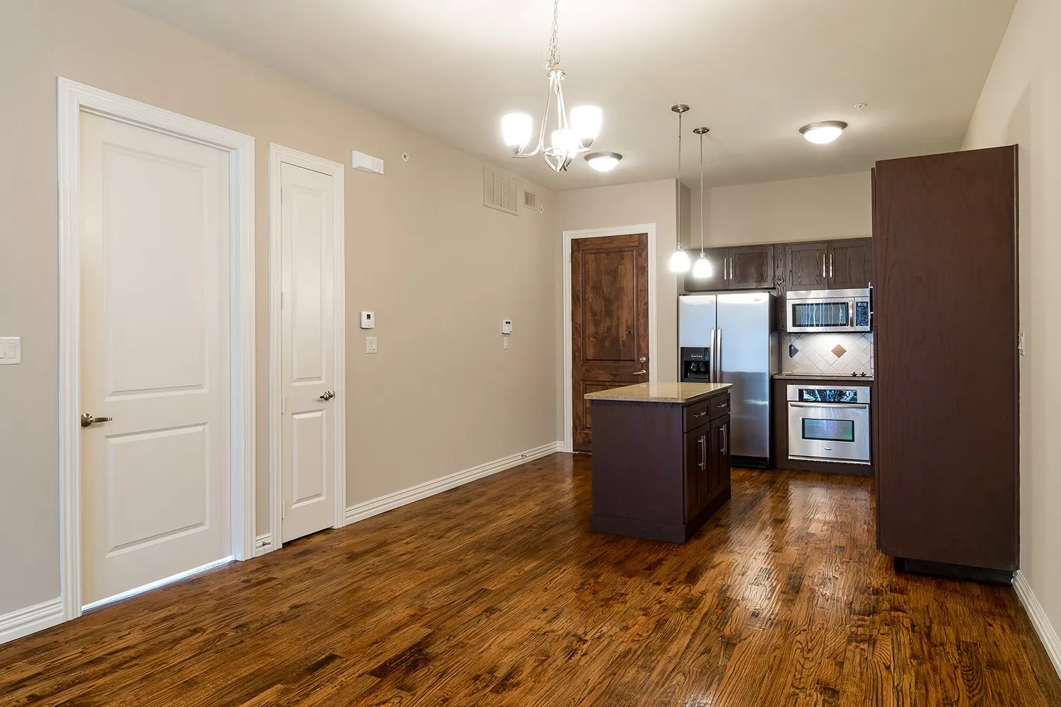 Kitchen with dark wood finish cabinetry, a kitchen island, stainless steel appliances, and suspended lighting