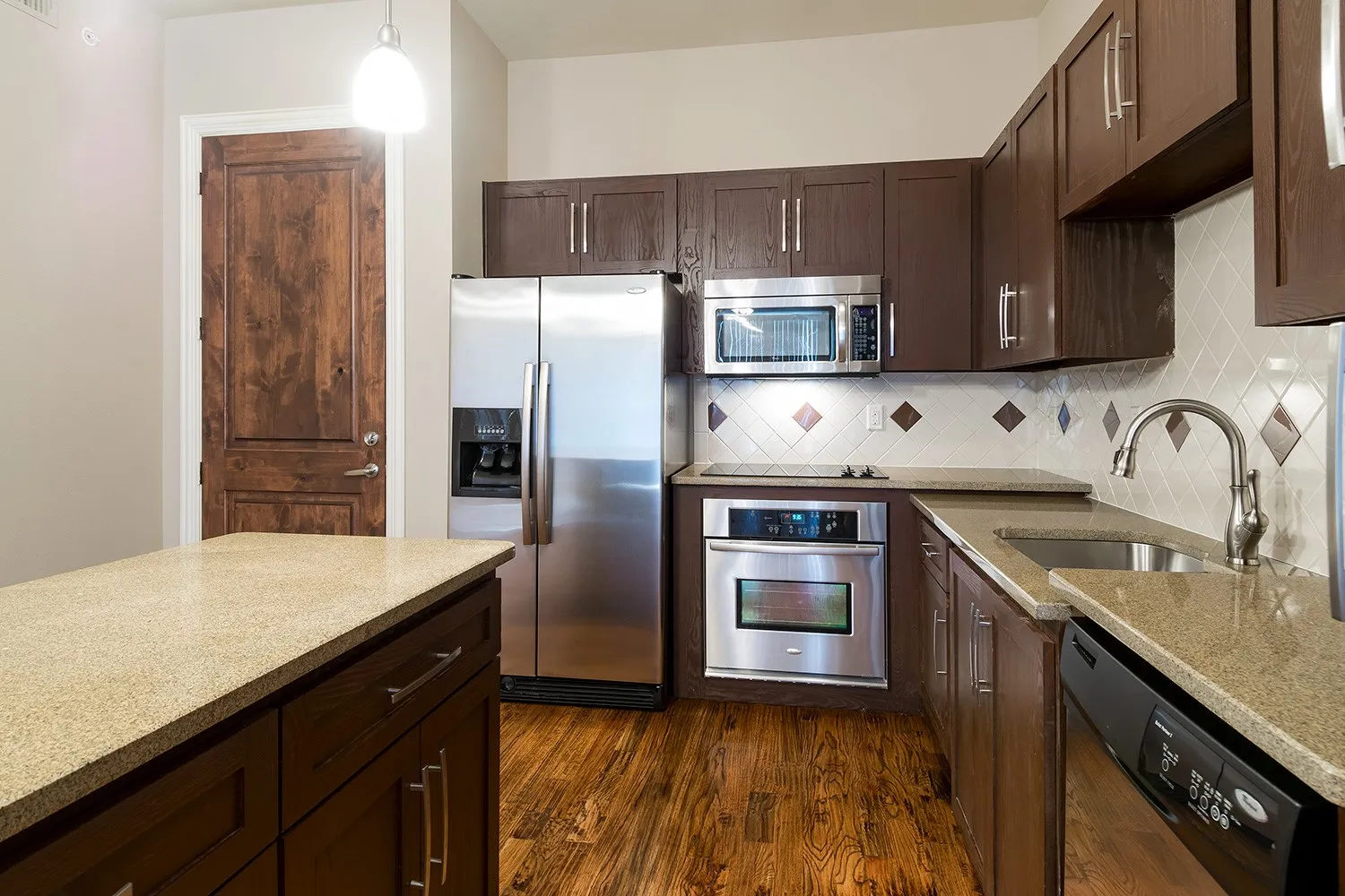 Kitchen featuring dark wood finish cabinets, stainless steel appliances, light stone countertops, and dark wood-style floors