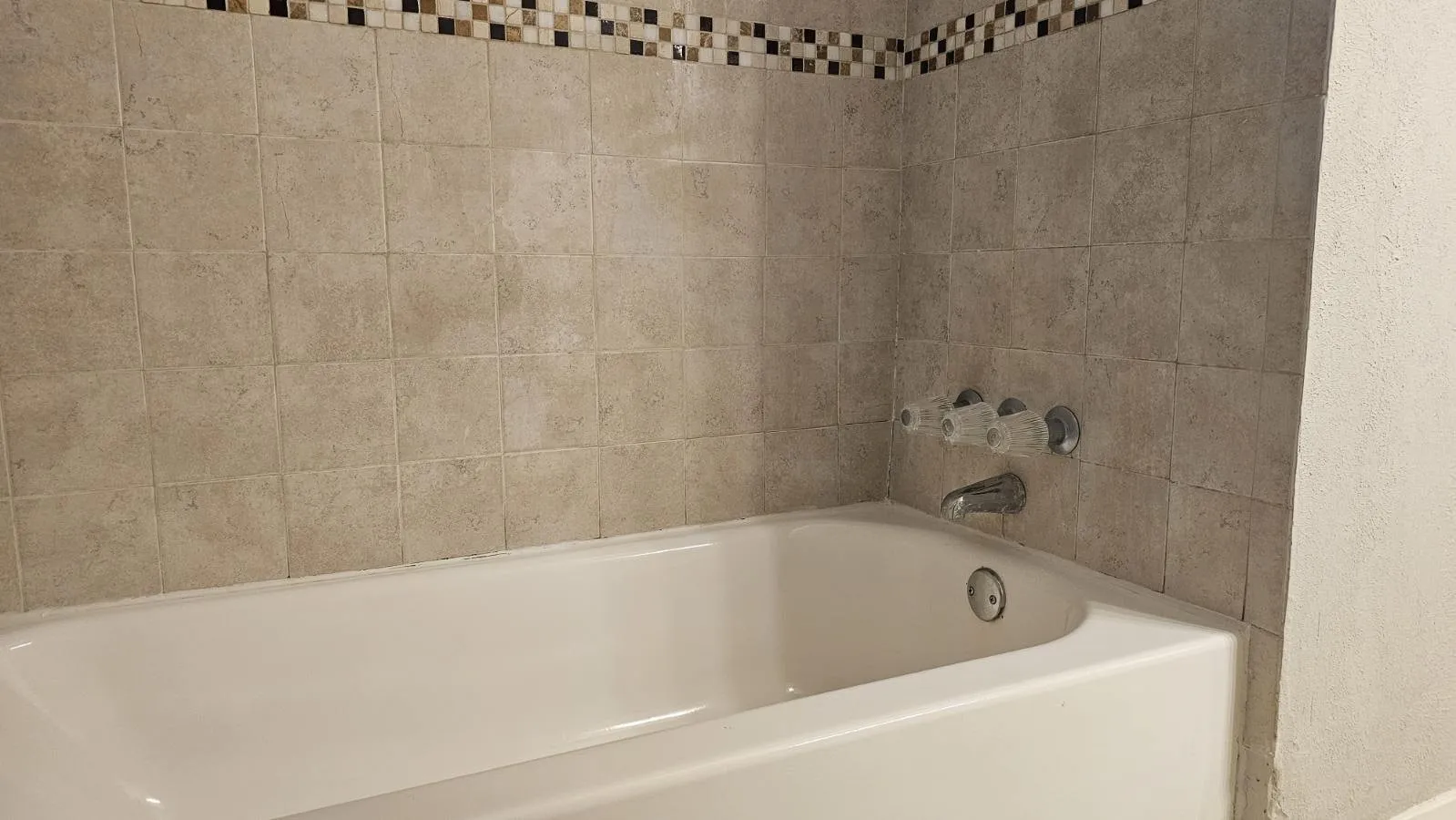 White bathtub with a tile surround and decorative mosaic border