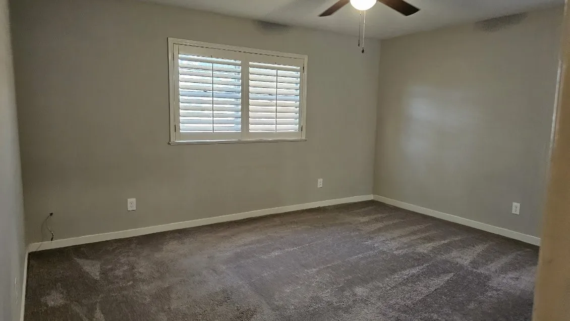 Carpeted flooring, window with plantation shutters, ceiling fan with integrated lighting, and neutral wall tones