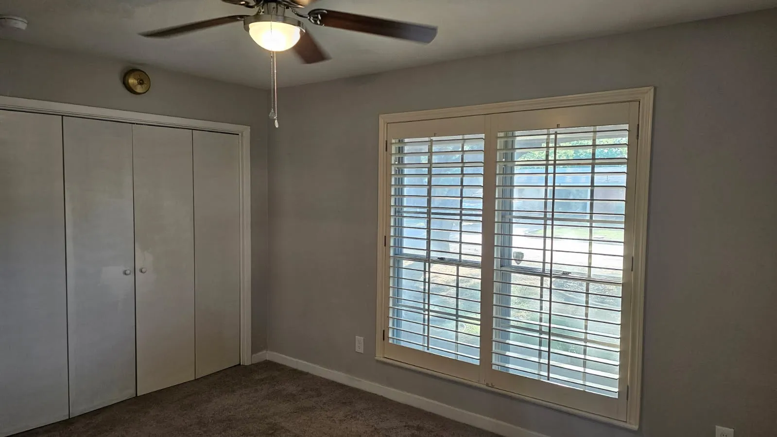 Window with plantation shutters, ceiling fan with integrated lighting, and carpeted flooring