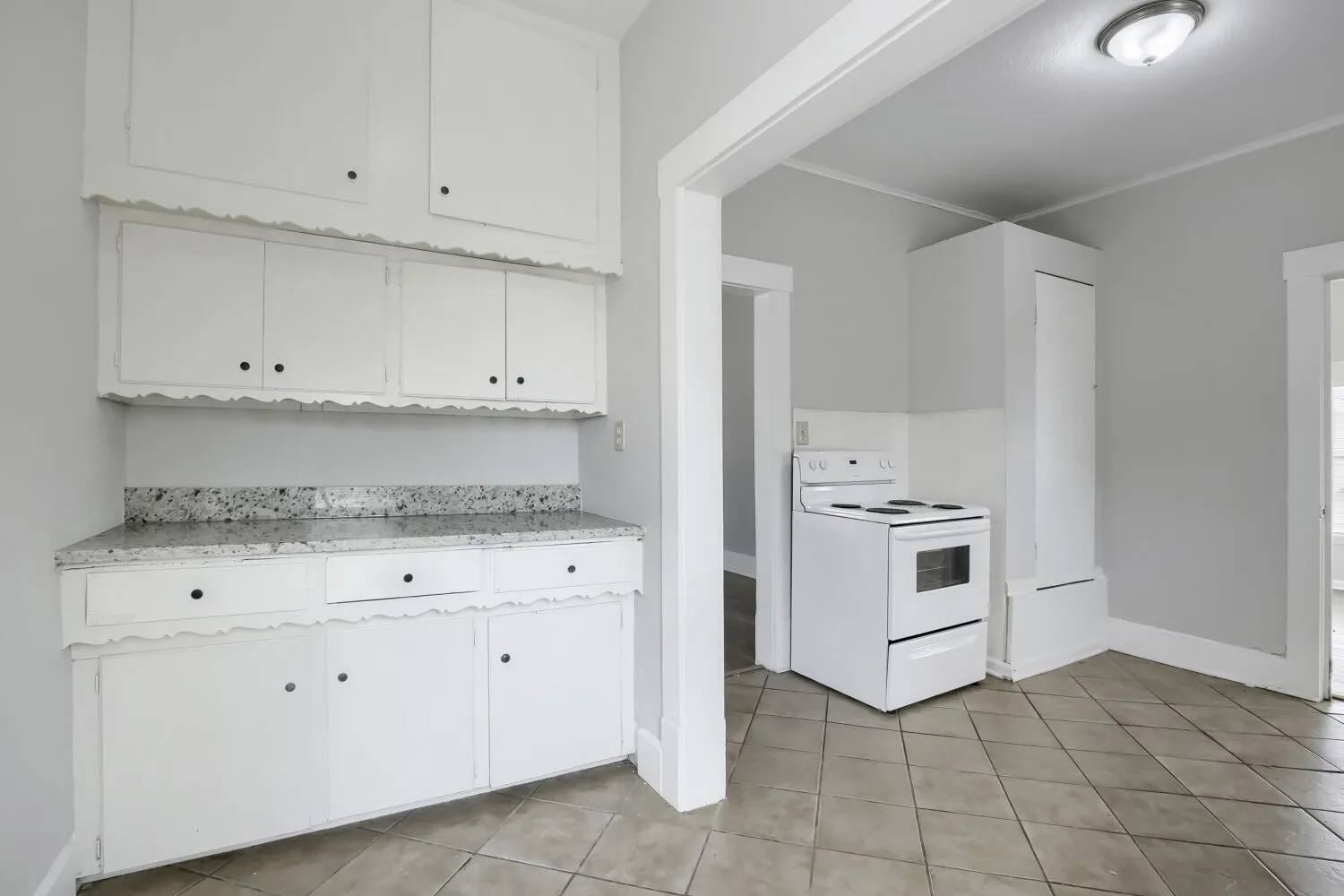 White cabinetry, speckled countertop, white electric range, and gray tiled flooring