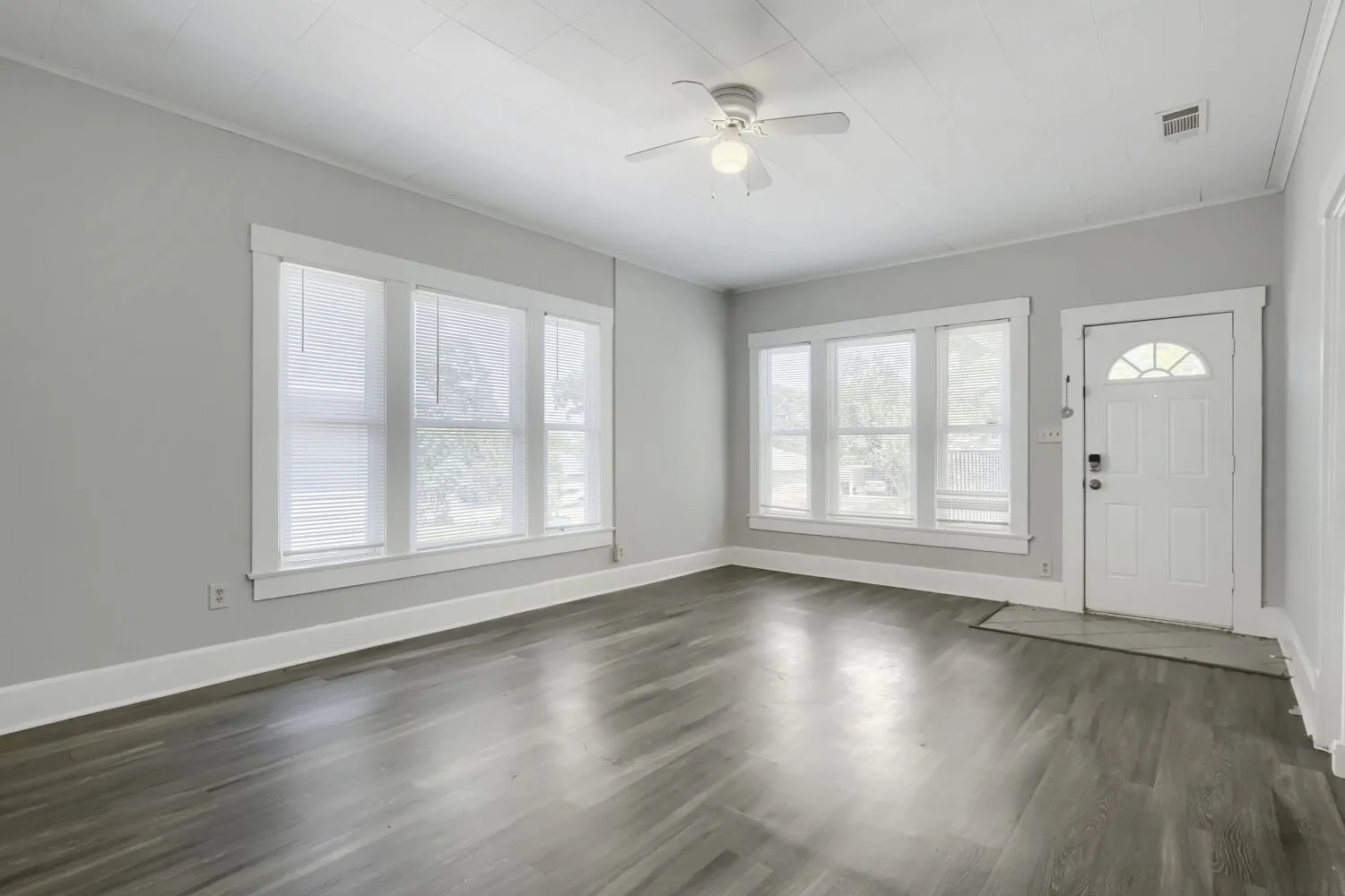 Bright, open living space flooded with natural light through multiple multi-pane windows and glass-paneled entry door