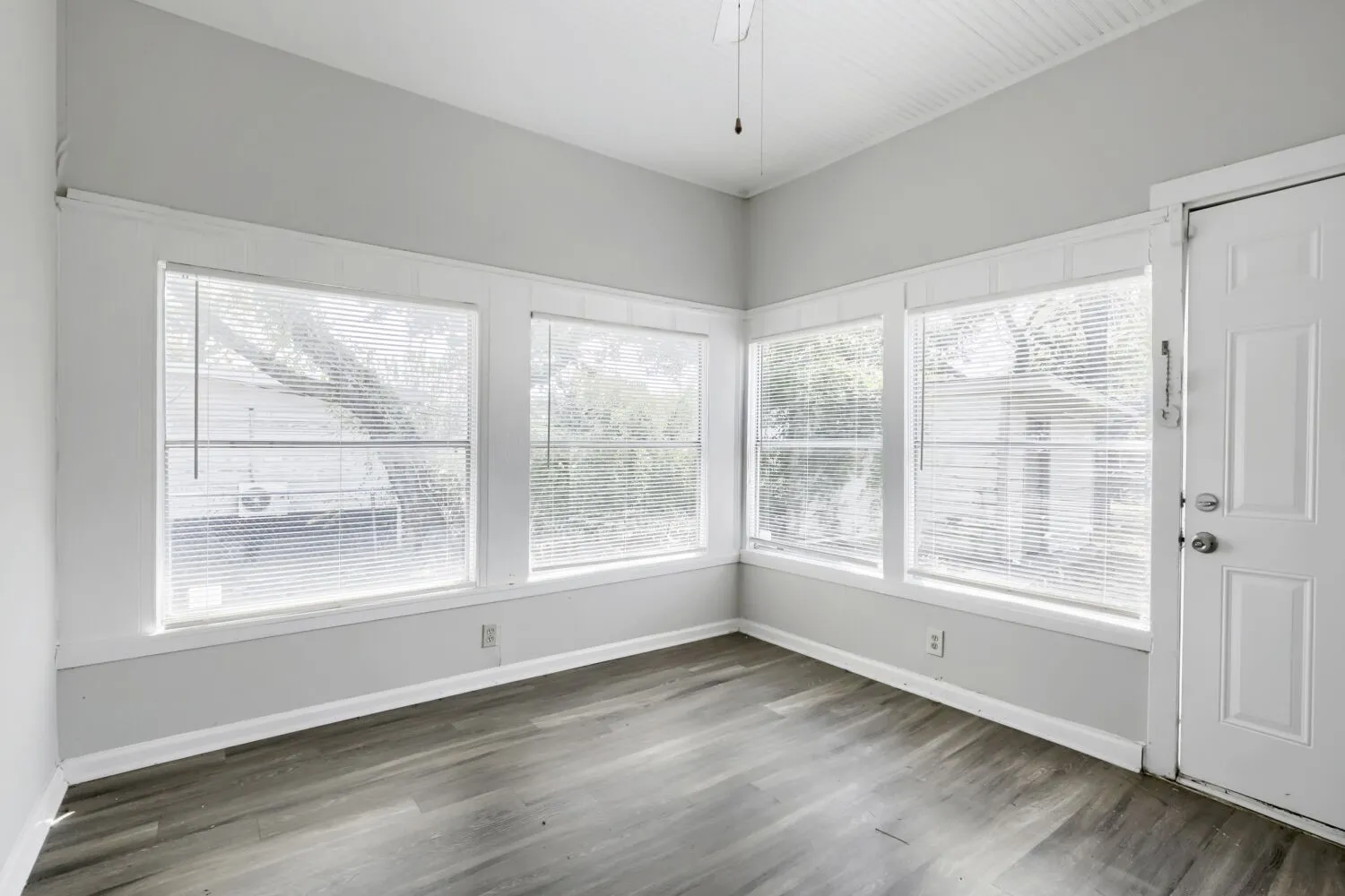 Wood-finish flooring, multiple windows, white door, light gray wall paint, and a white ceiling