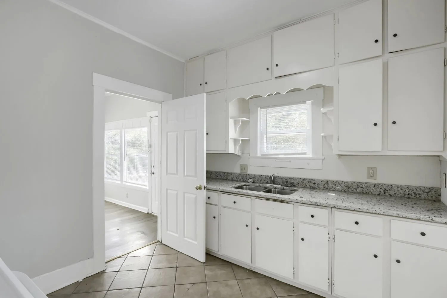 White cabinetry with a double basin sink, speckled countertop, and tiled flooring