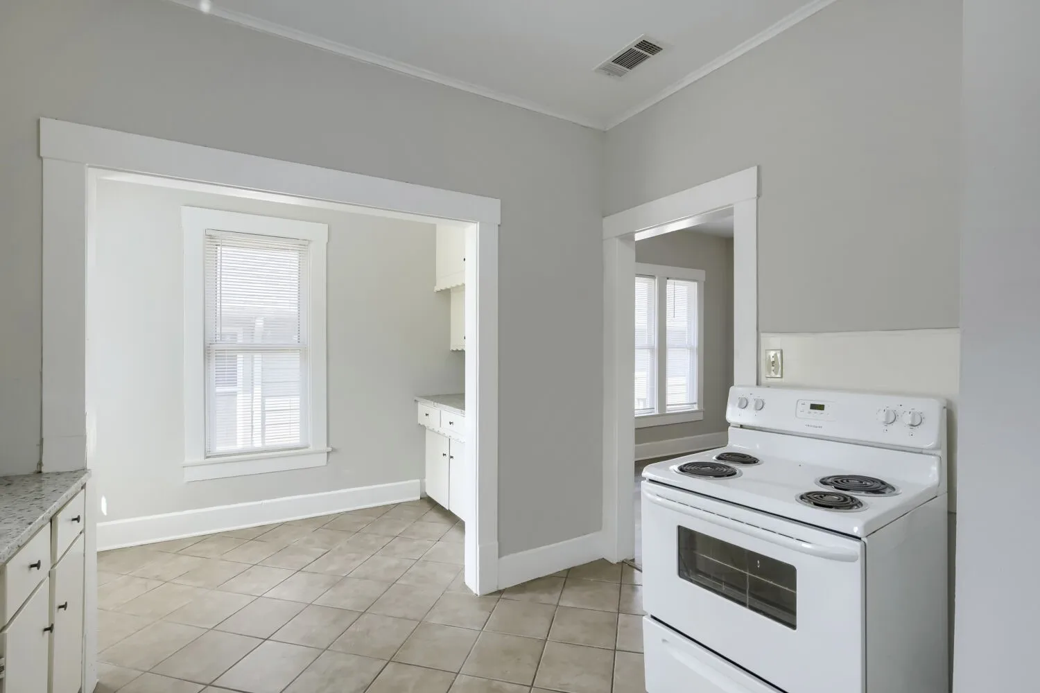 Spacious kitchen featuring white coil-top electric range, tile flooring, and abundant natural light from multiple windows