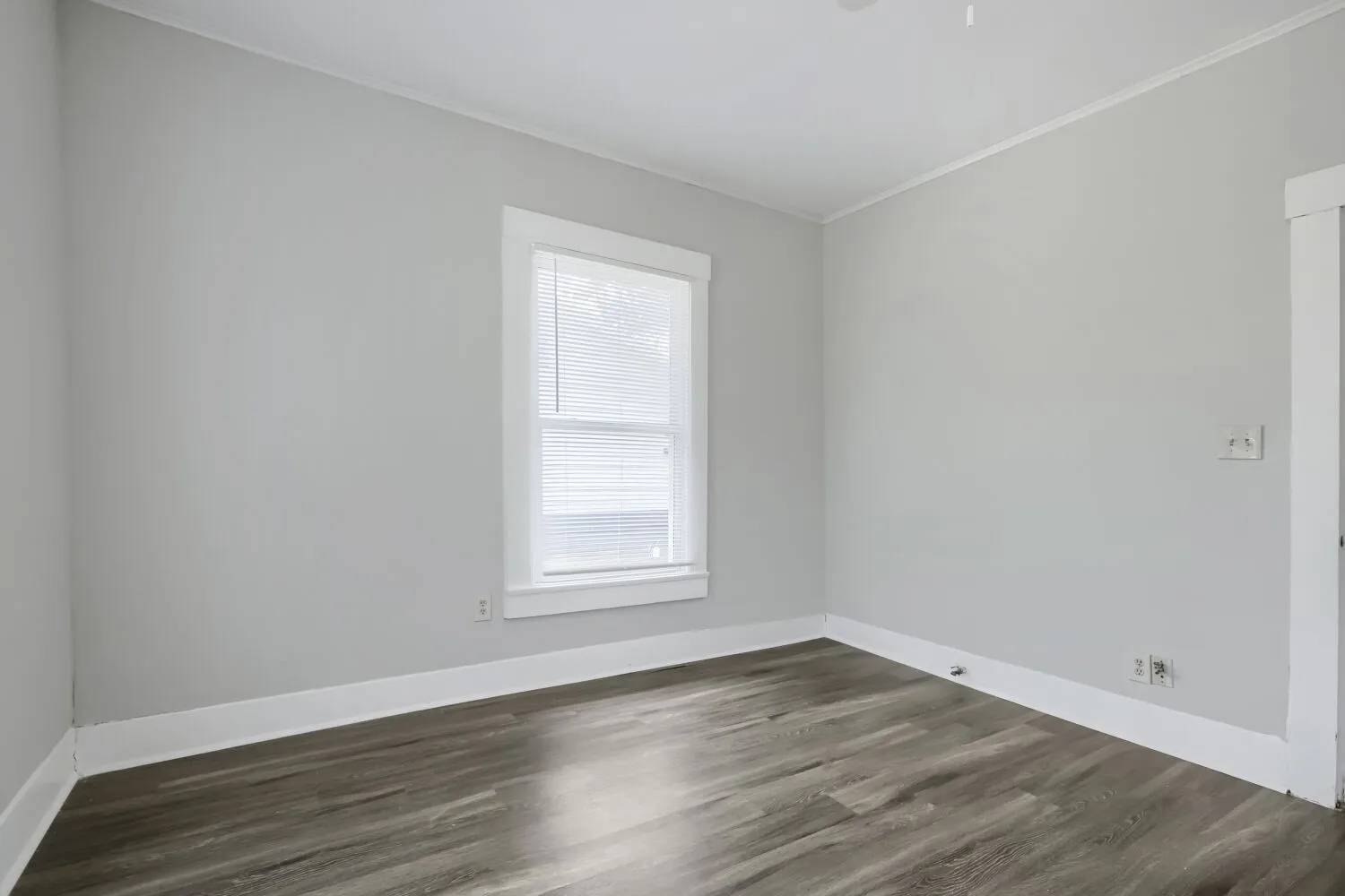 Interior room with light gray painted walls, a single window with white blinds, and wood-finish flooring