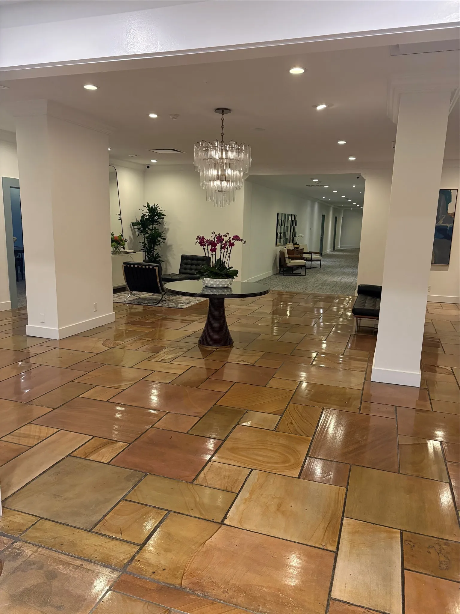 Polished natural stone flooring, recessed ceiling lighting, a tiered glass chandelier, and white-painted columns
