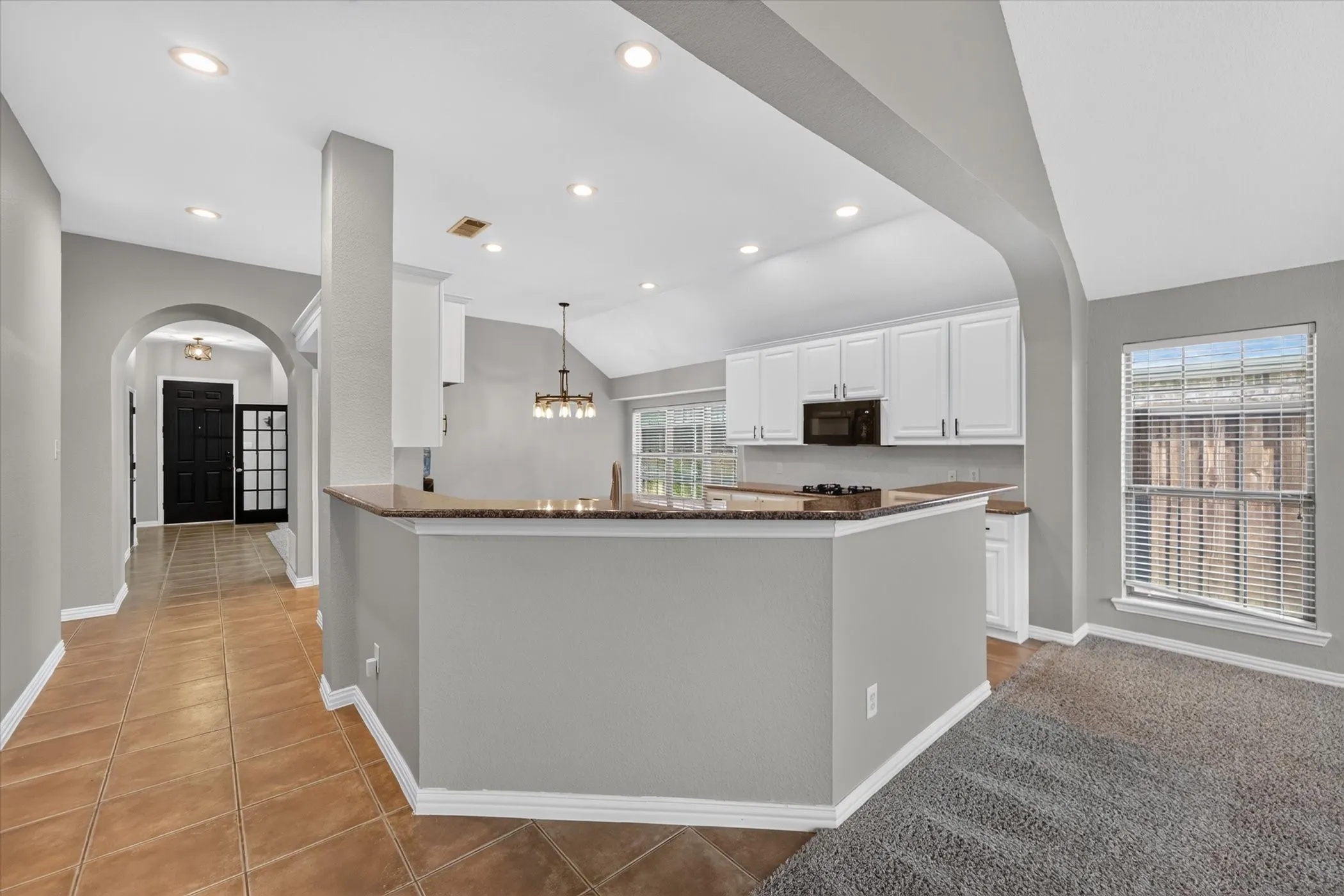 Kitchen featuring white cabinetry, dark countertops, a built-in microwave, and a decorative pendant light fixture