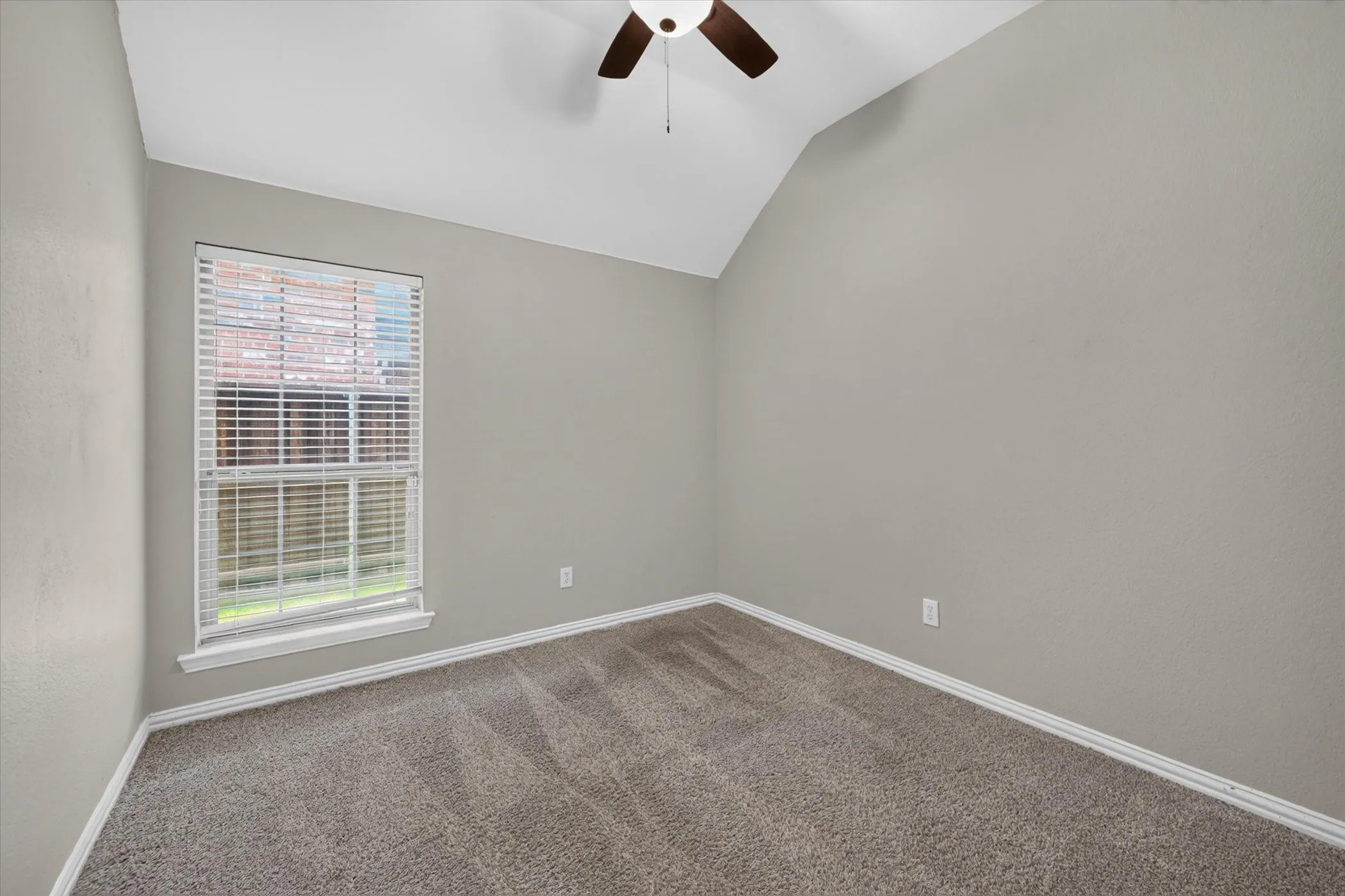 Vaulted ceiling with an attached ceiling fan, single window with blinds, light gray wall finish, and gray carpet flooring