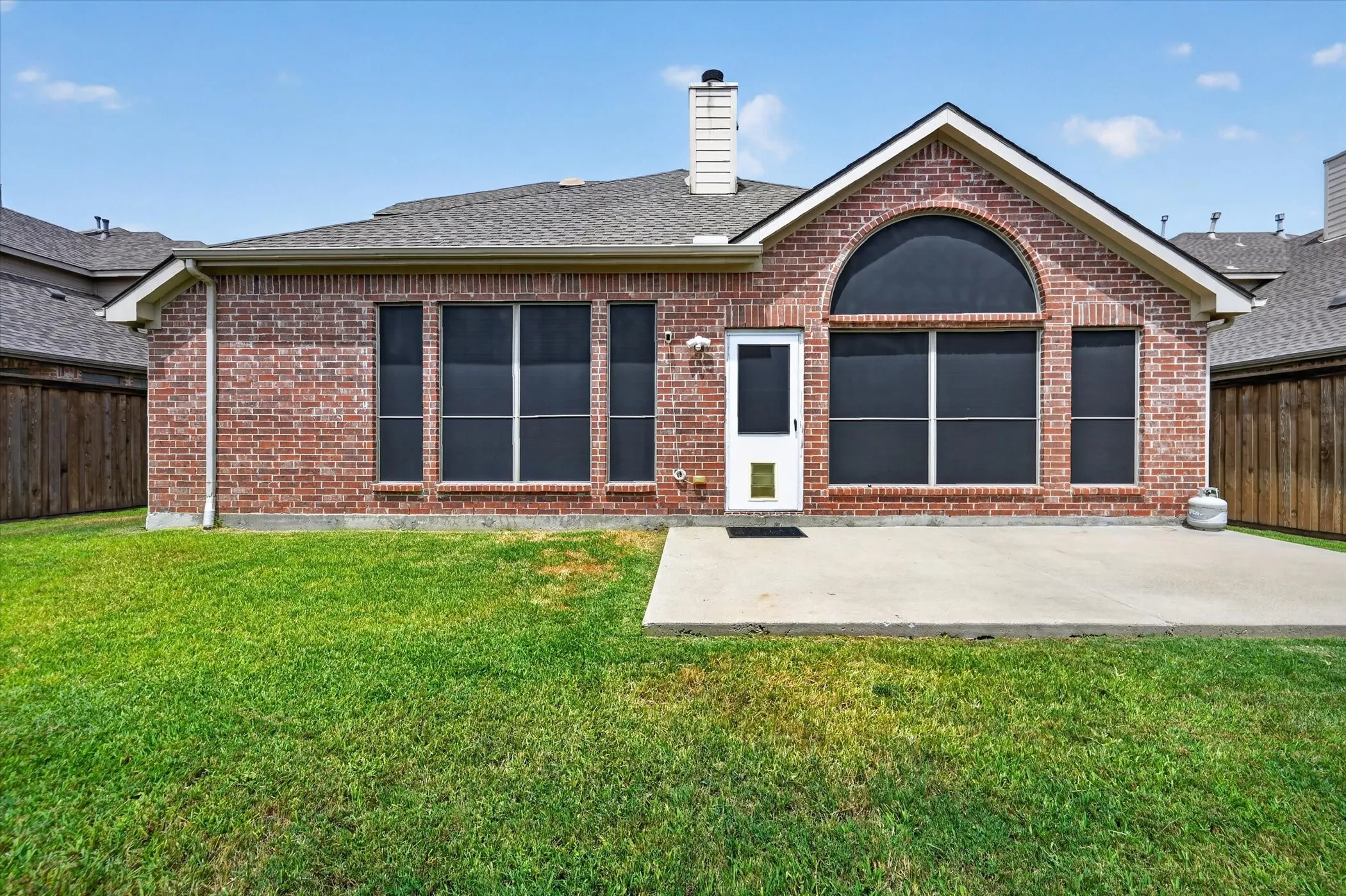 Brick exterior with an arched window, multiple large windows, and a concrete patio