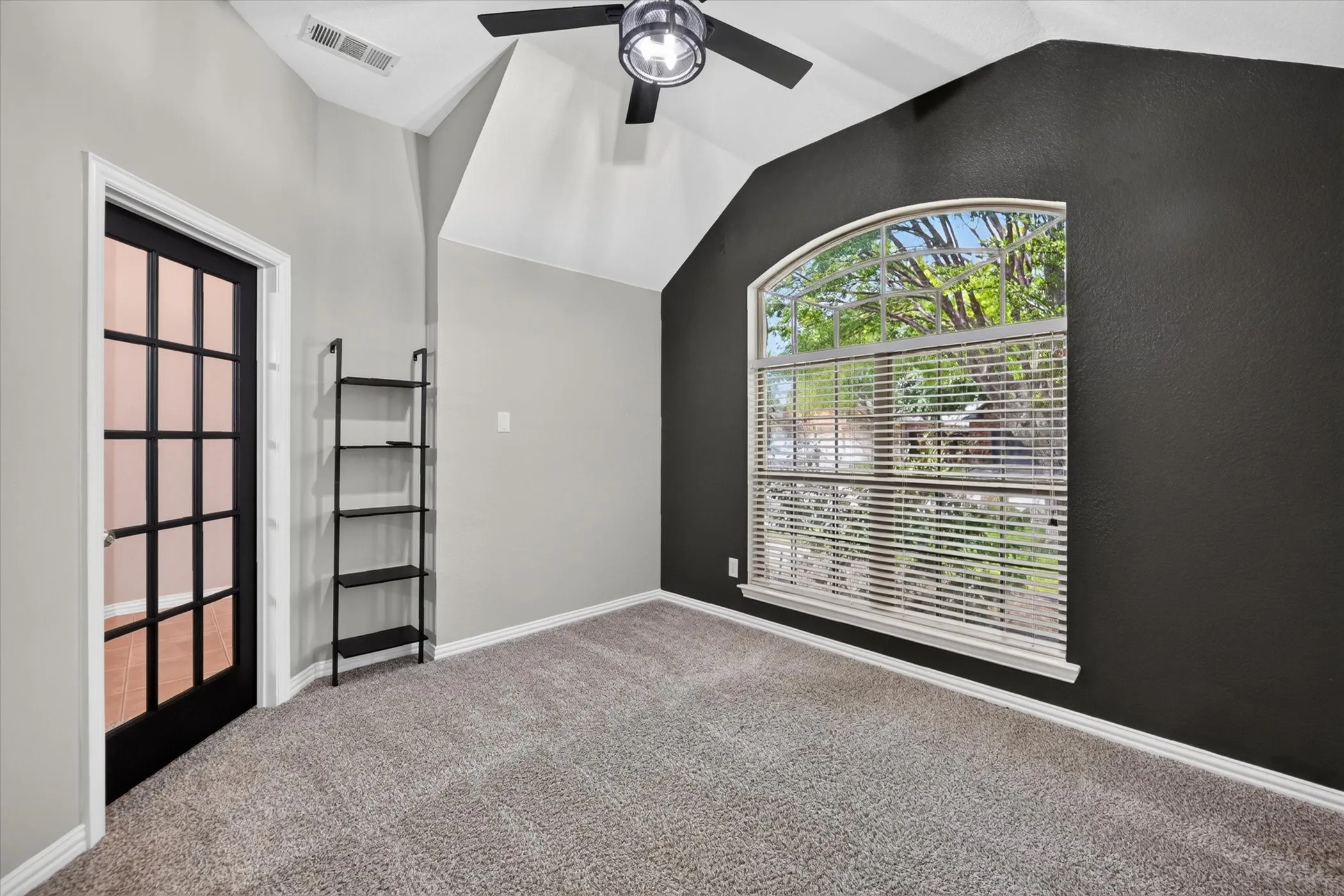 Vaulted ceiling featuring a ceiling fan, arched window with blinds, French paneled door, and carpet flooring
