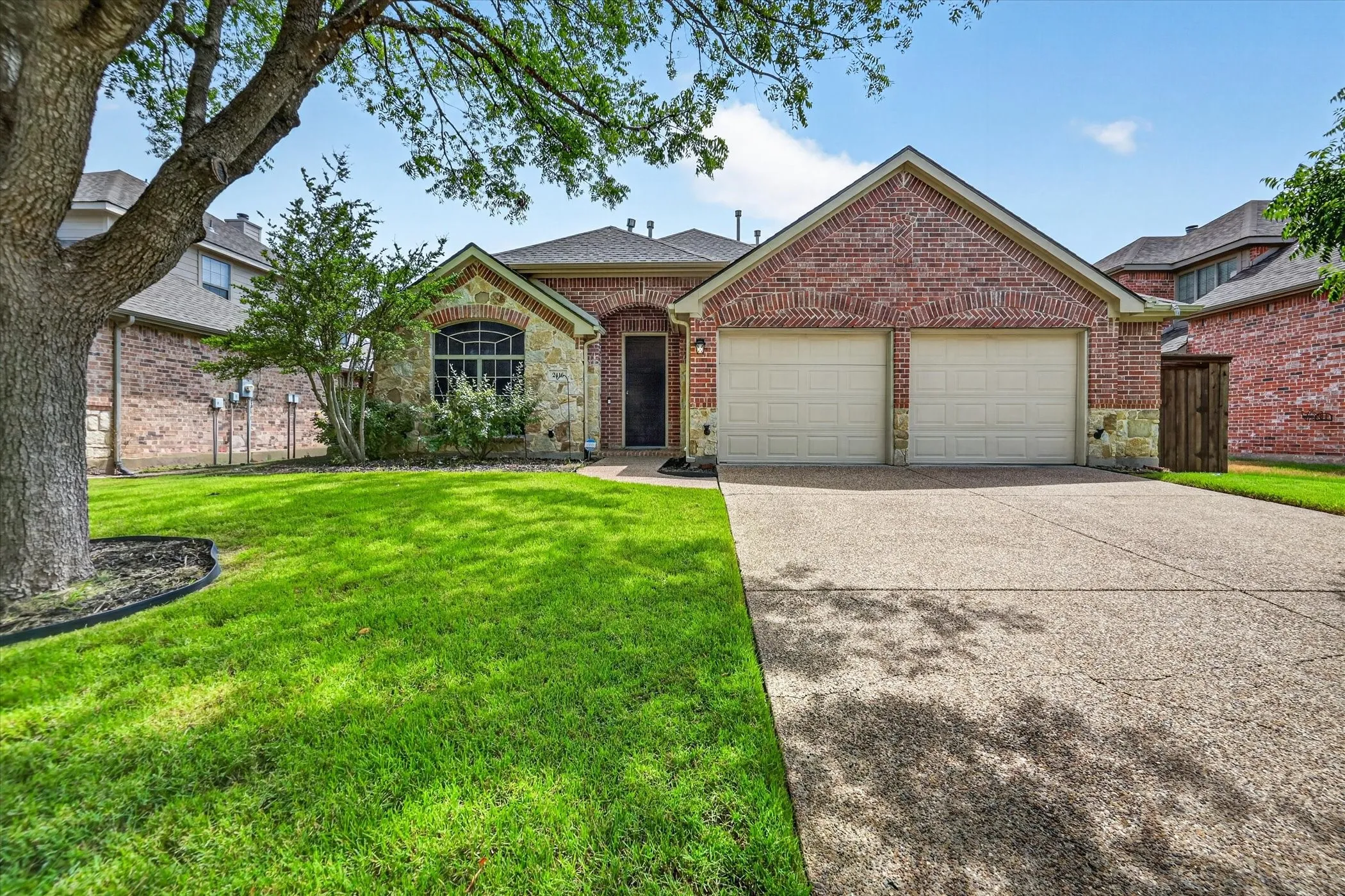Brick and stone facade, two-car garage, concrete driveway, arched window, and mature tree