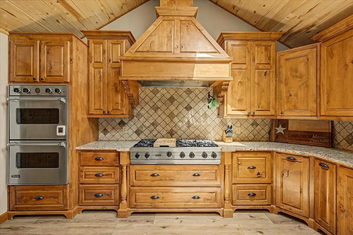 Wood-finish vaulted ceiling, custom wood cabinetry, stainless steel double wall ovens, gas range, and granite-style countertops