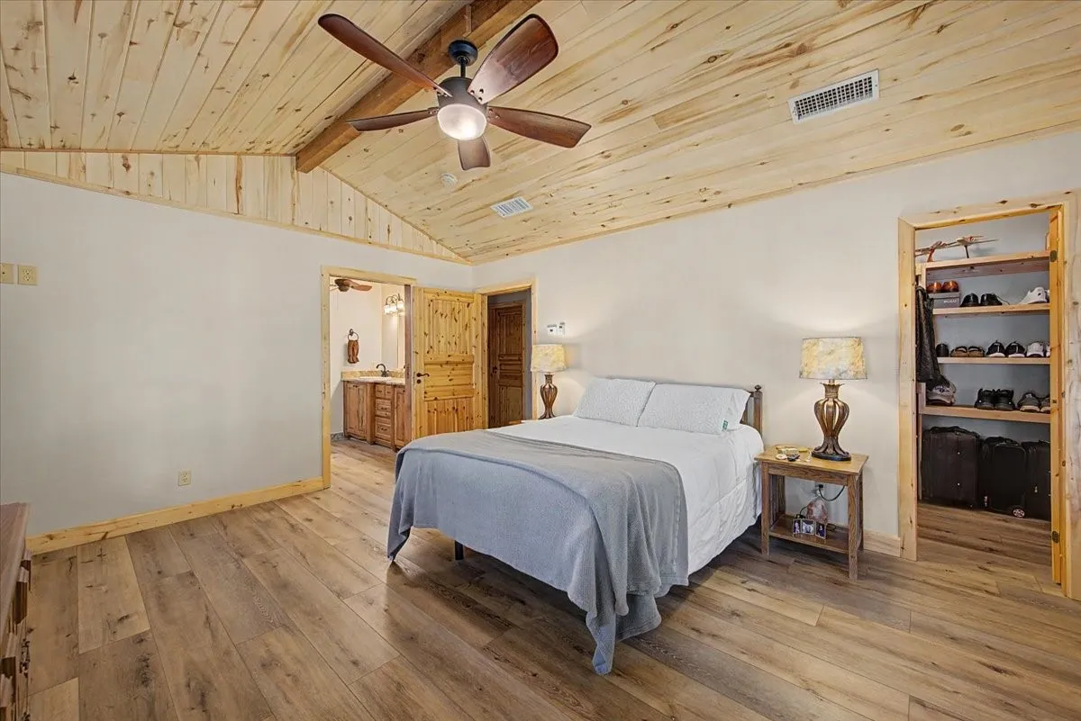 Vaulted wood-paneled ceiling with exposed beam, wood-finish flooring, built-in open shelving, and a ceiling fan