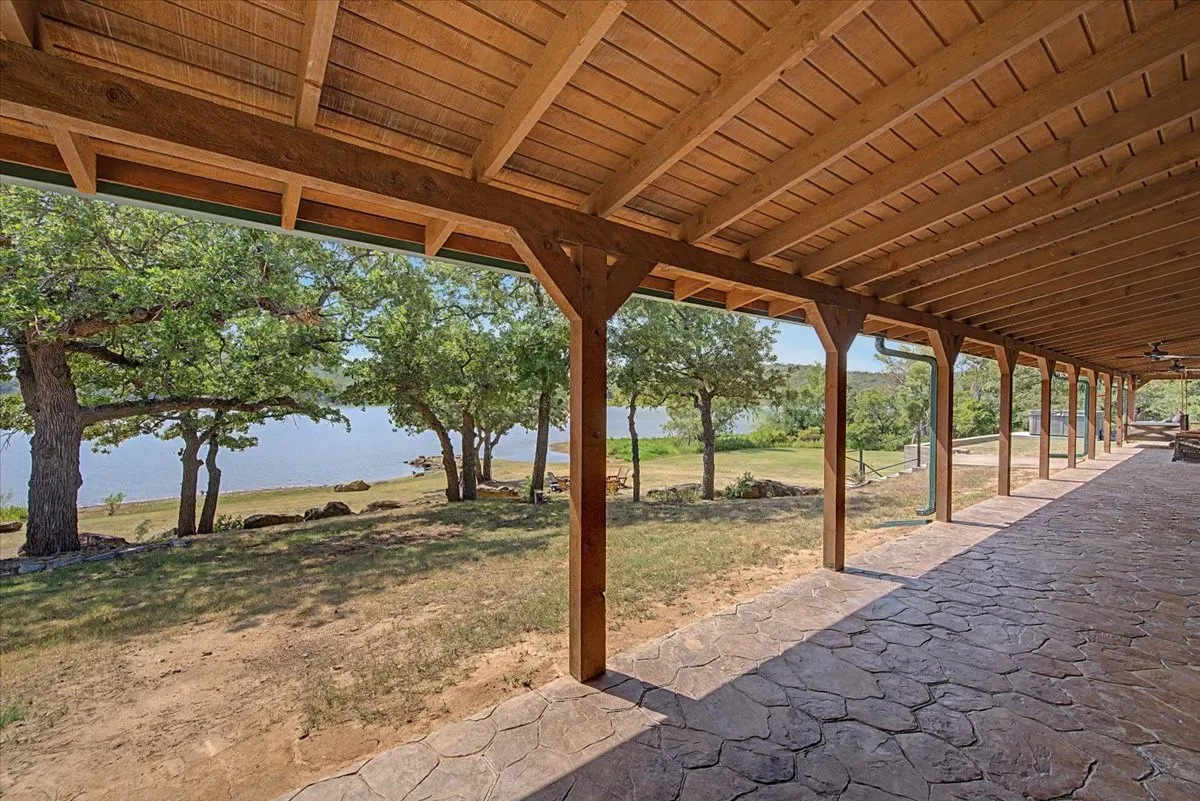 Expansive covered outdoor living space featuring a wood-finish ceiling, exposed support beams, and a stamped concrete patio