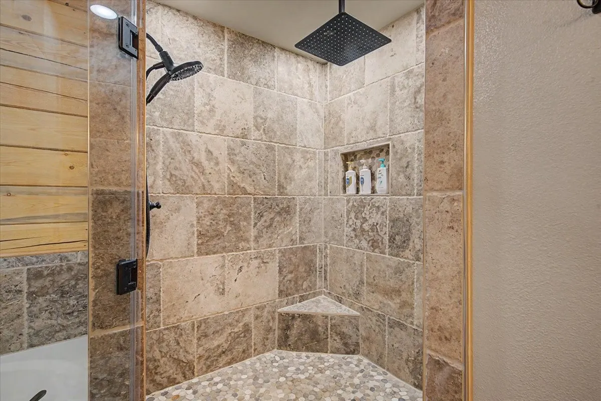 Tiled shower enclosure featuring a corner bench, recessed shelf, and dual showerheads
