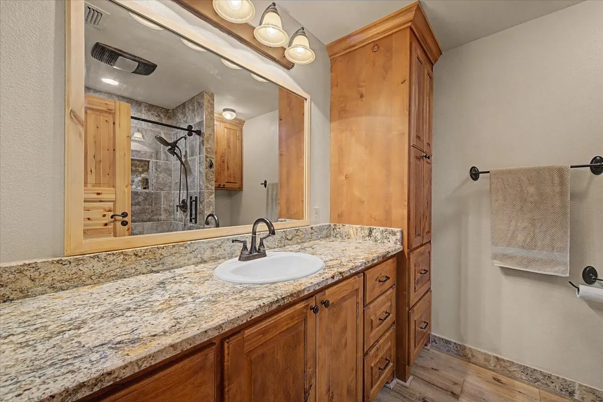 Wood-finish vanity with an integrated sink, stone-finish countertop, wood-finish mirror frame, and built-in wood-finish cabinetry