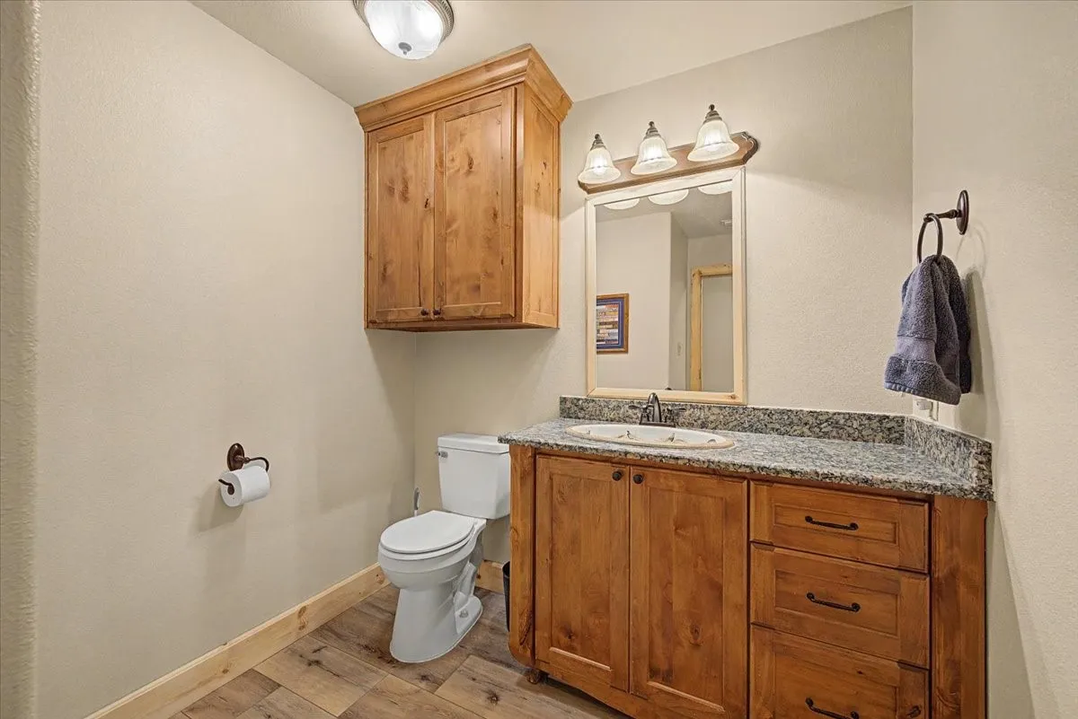 Wood-finish flooring, wood cabinetry, stone-finish countertop, and a built-in vanity with integrated sink