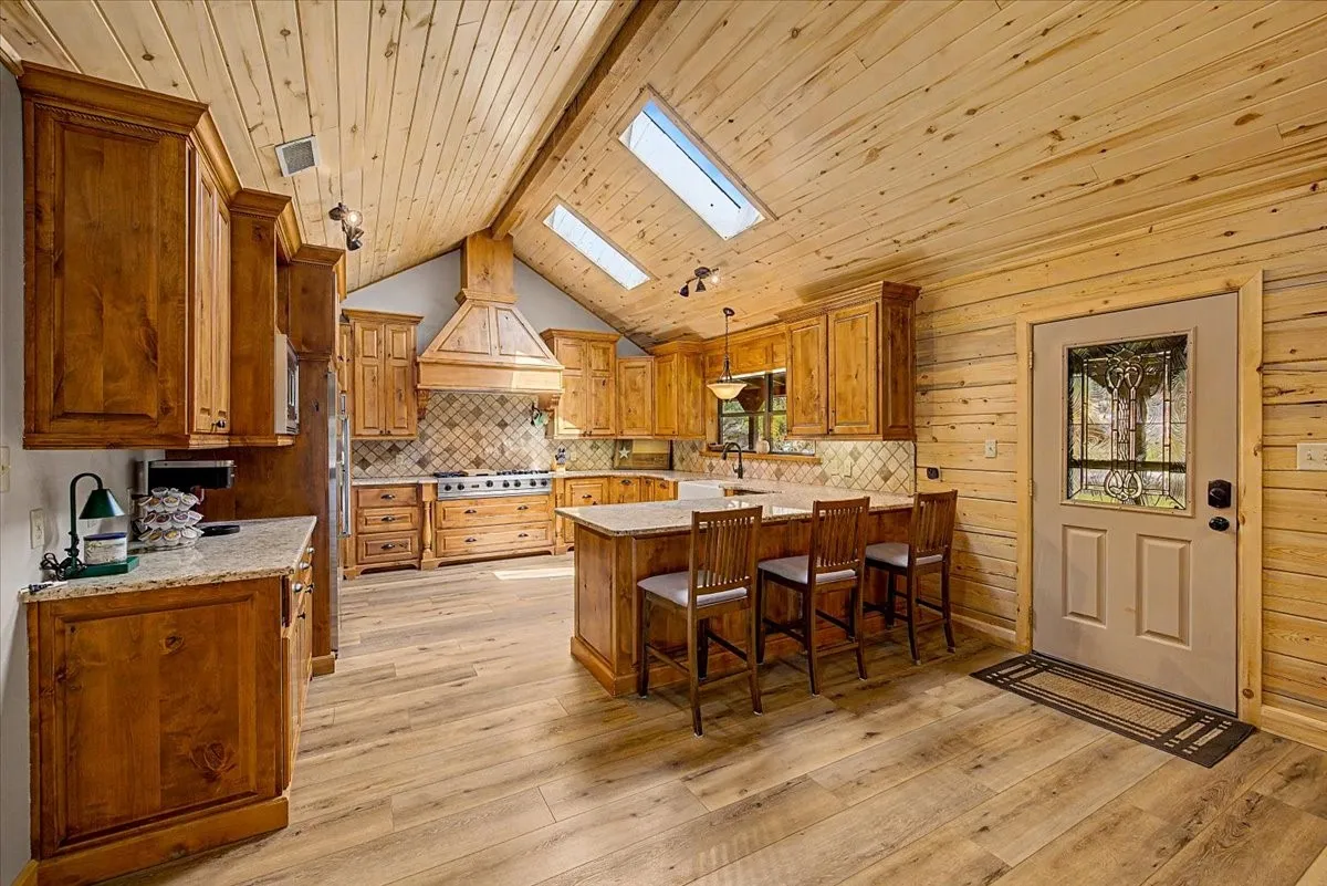 Vaulted wood-paneled ceiling with skylights, wood-finish flooring, custom wood cabinetry, kitchen island with seating, and a decorative tile backsplash