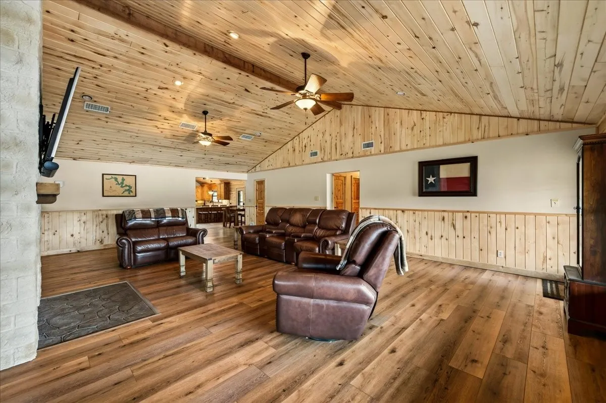 Vaulted wood-paneled ceiling, wood-finish flooring, wood wainscoting, white stone-finish fireplace surround, and recessed lighting