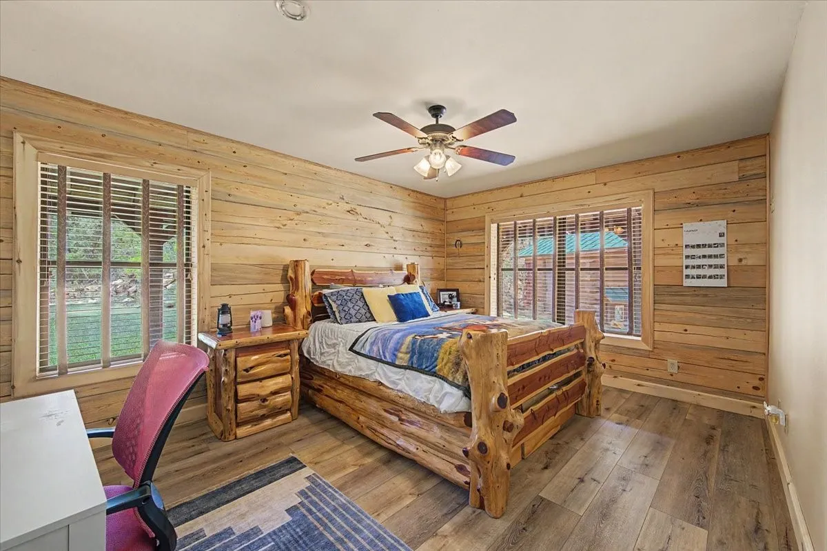 Wood-finish flooring, wood-paneled walls, and a ceiling fan with integrated lighting