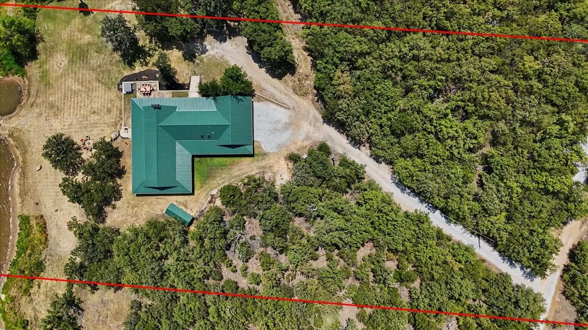 Property with a green metal roof, surrounded by extensive natural vegetation, and featuring a pond