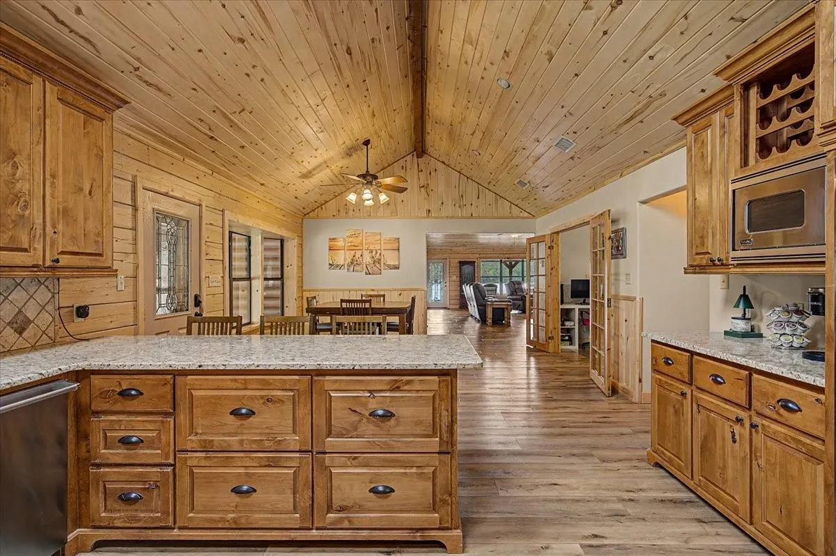 Vaulted wood-paneled ceiling, wood-finish flooring, wood cabinetry with dark hardware, stone countertops, and built-in microwave