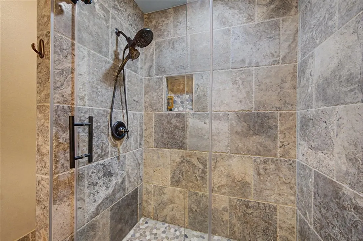 Tiled shower enclosure featuring a fixed showerhead, handheld shower fixture, and a built-in niche