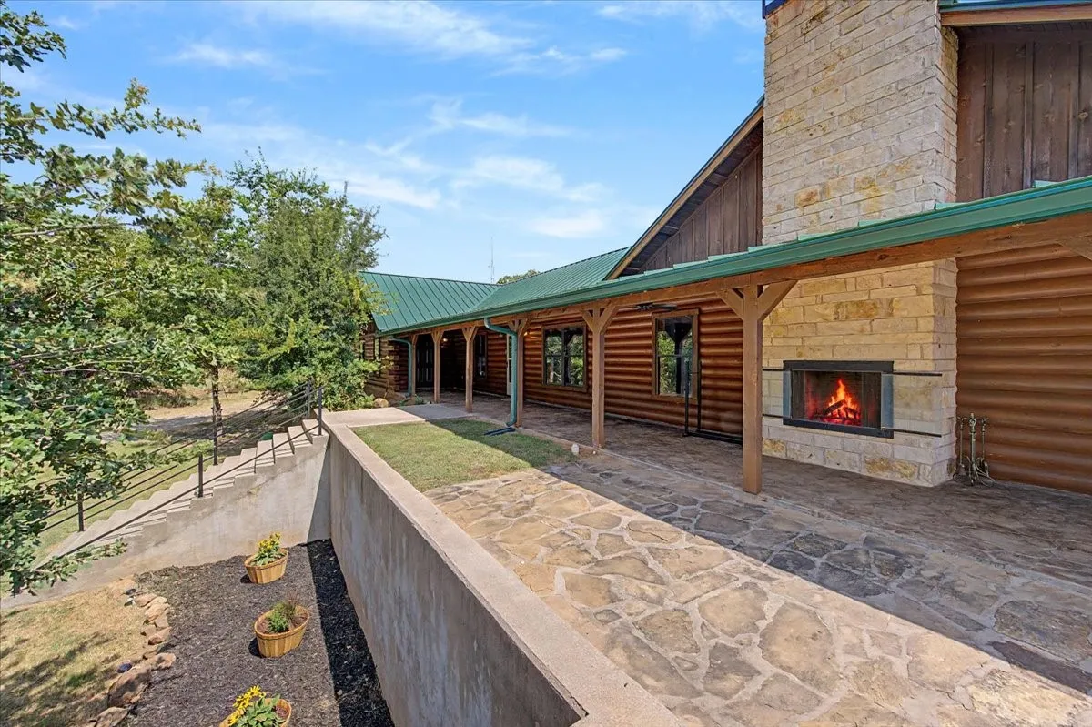 Log cabin exterior with an expansive stone patio, covered porch, and integrated stone fireplace