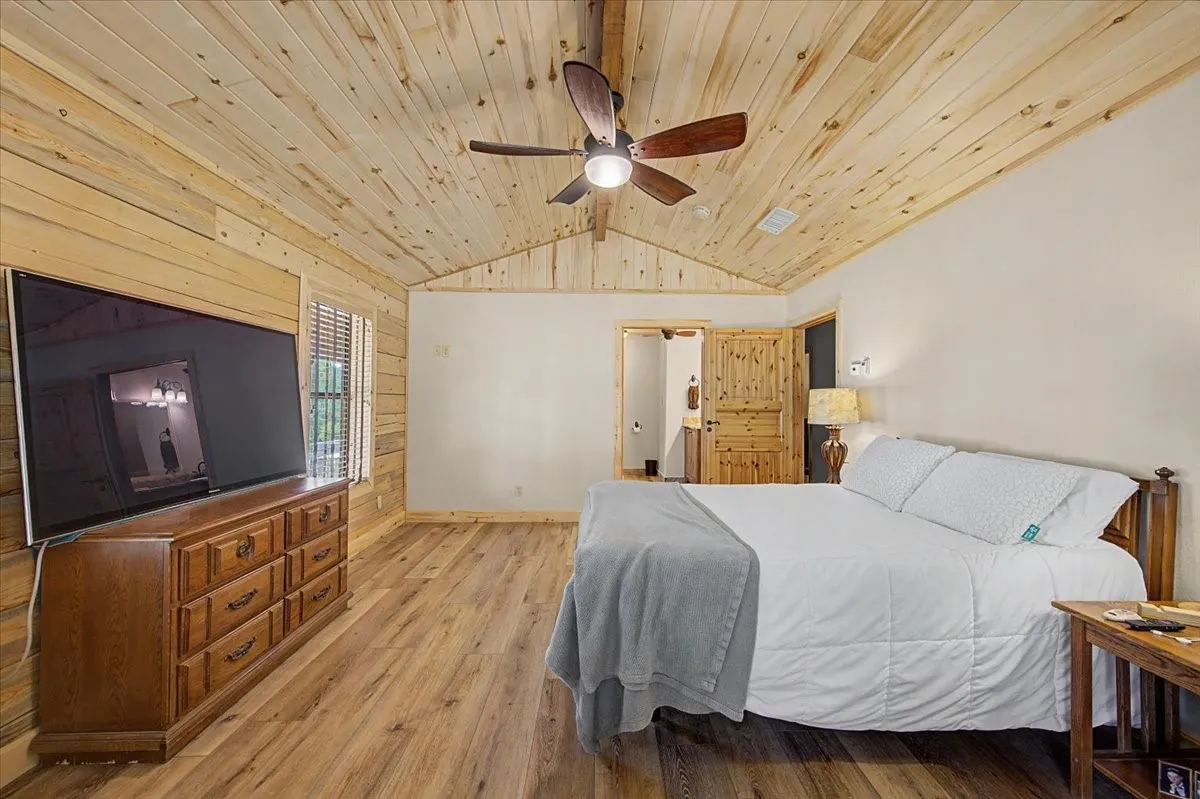 Vaulted wood-paneled ceiling with a ceiling fan, wood-finish flooring, and natural wood wall accents