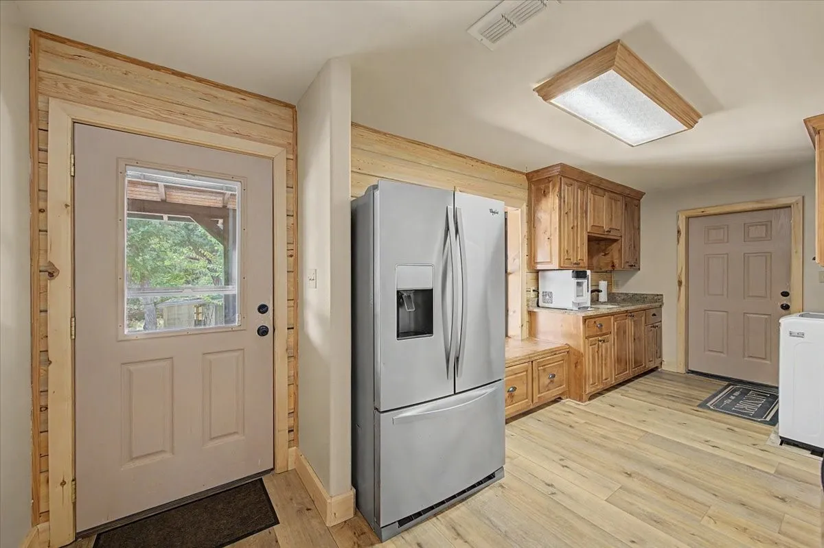 Wood-finish flooring, wood cabinetry with stone-look countertops, stainless steel refrigerator, and recessed ceiling lighting