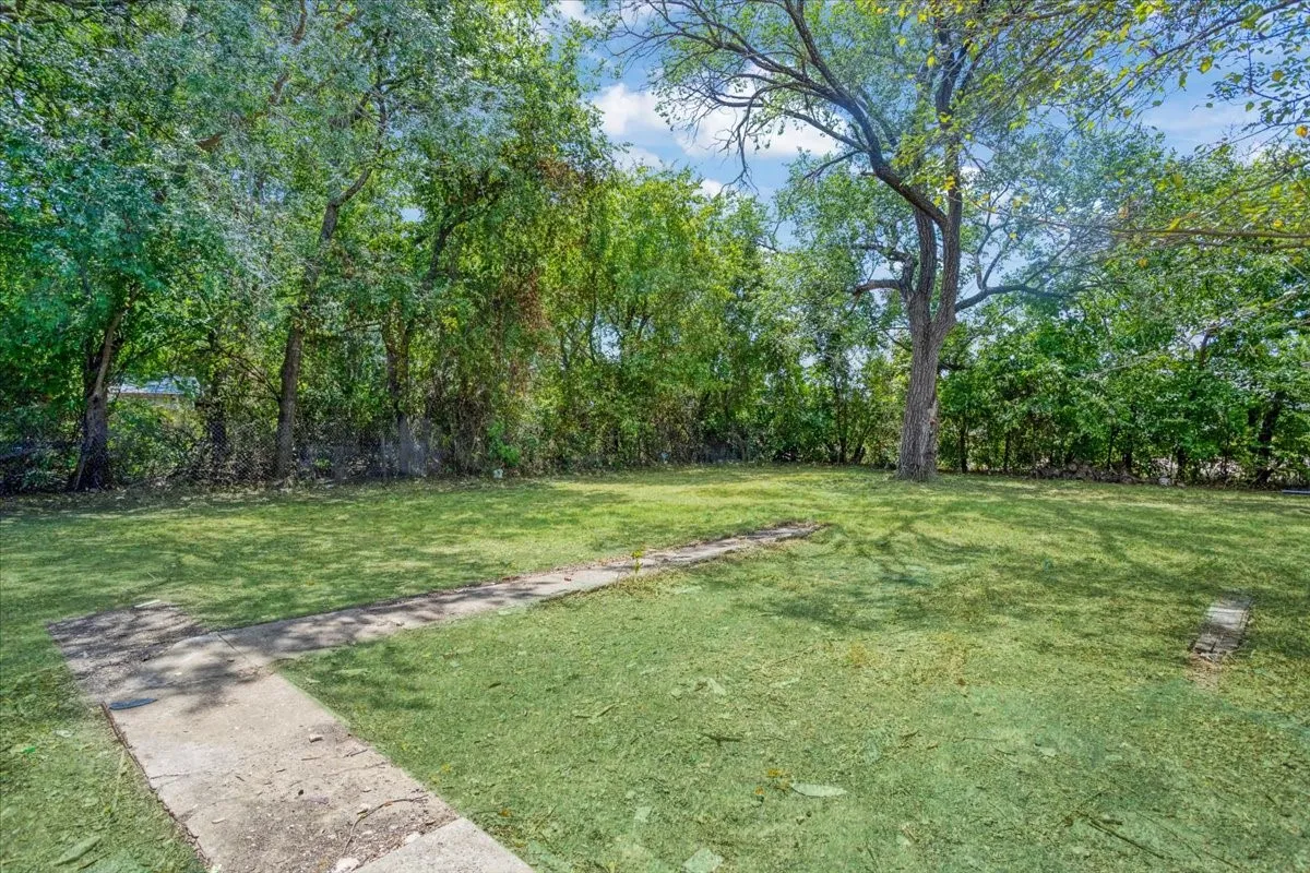 Expansive grassy yard with mature trees and a concrete pathway