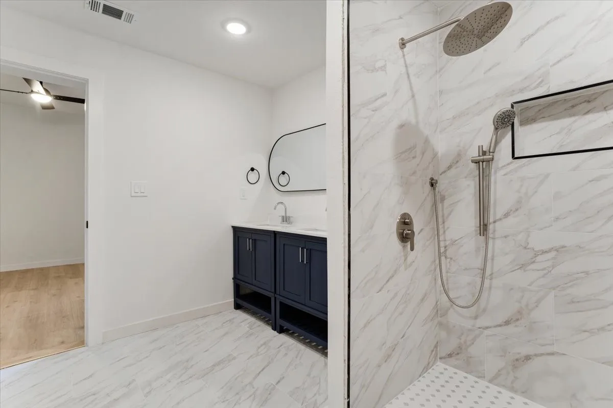Walk-in shower with a rain showerhead, handheld shower fixture, and a built-in niche
