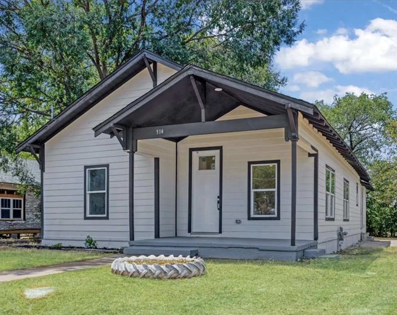 Covered front porch with dark-painted wood columns, light-colored horizontal siding, and white trim windows