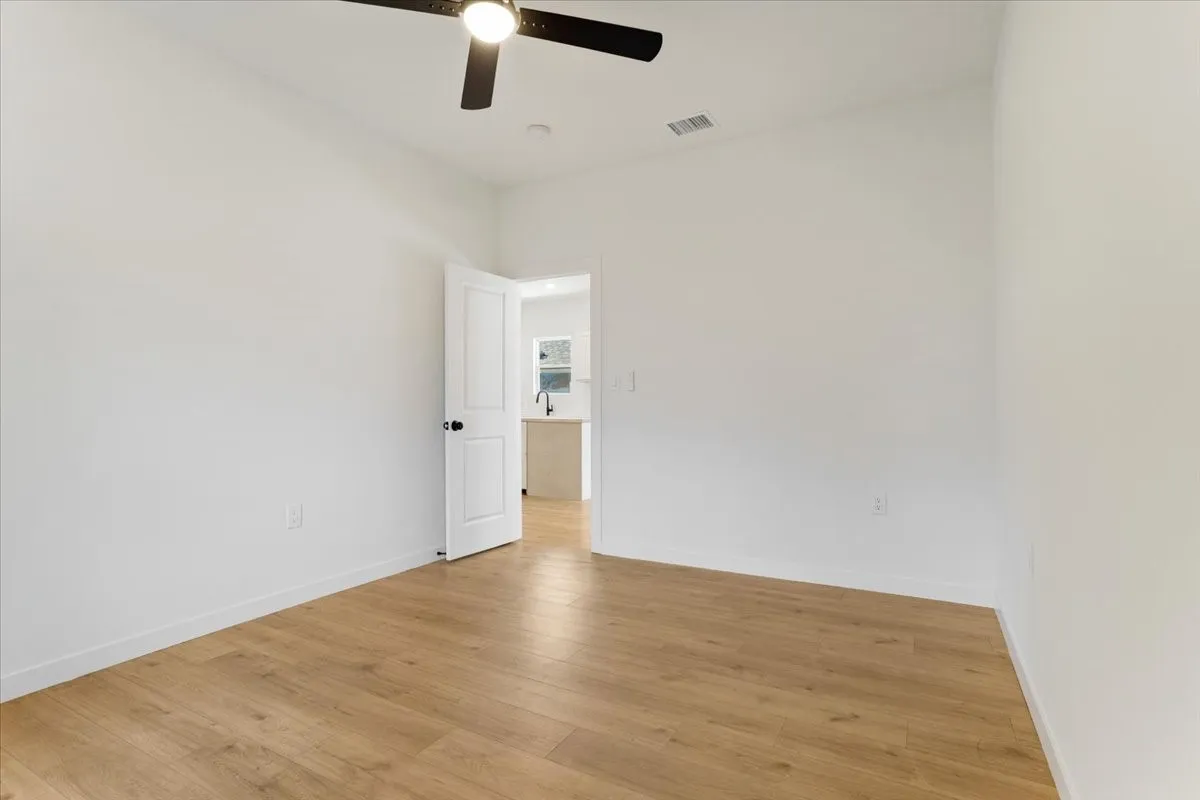 Wood-finish flooring with white baseboards, a white interior door with black hardware, and a ceiling fan with integrated lighting