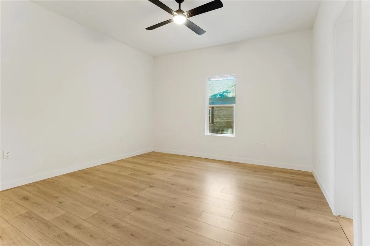 Vaulted ceiling, wood-finish flooring, white walls, rectangular window, and a ceiling fan