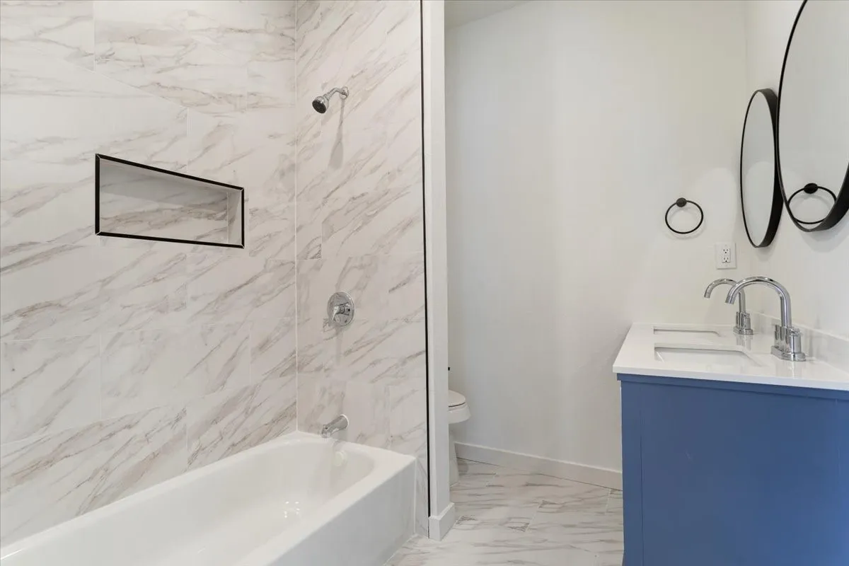 Bathtub and shower combination with a recessed niche, chrome fixtures, and white marble-patterned wall tile