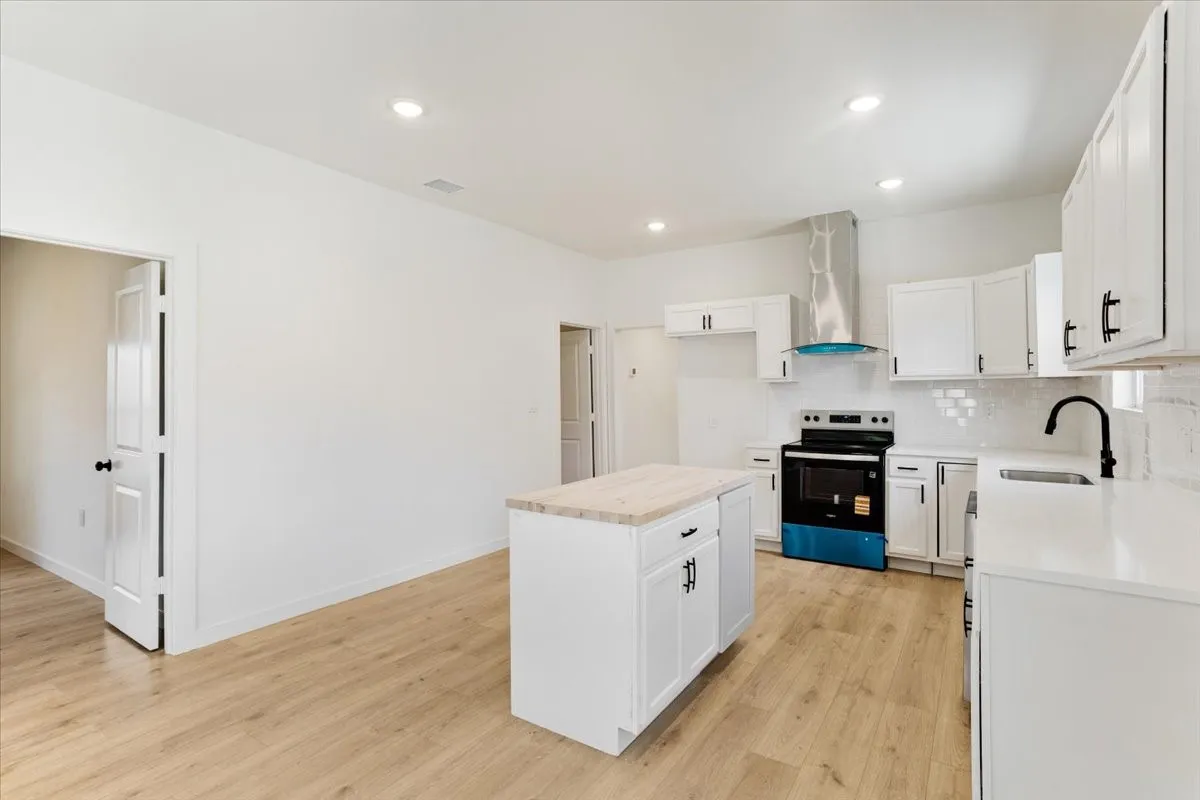 Kitchen featuring an island with countertop, white cabinetry with dark hardware, a stainless steel range hood, white subway tile backsplash, and light wood-finish flooring