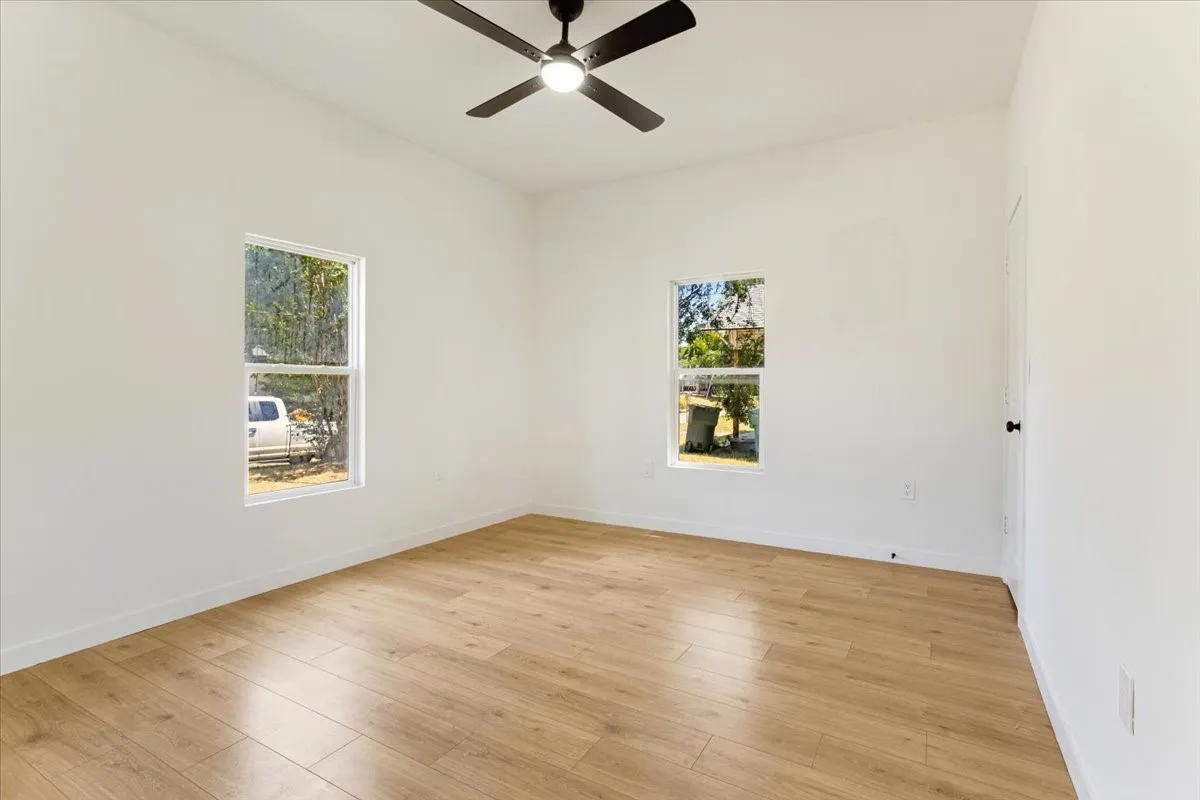 Wood-finish flooring, white walls, two double-hung windows, and a ceiling fan with integrated lighting