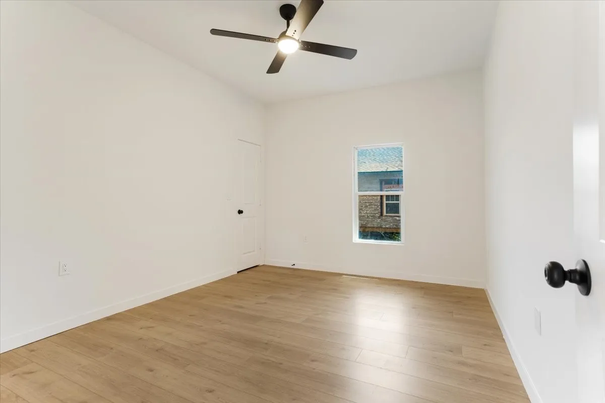 Vaulted ceiling with a black ceiling fan, wood-finish flooring, and a white framed window