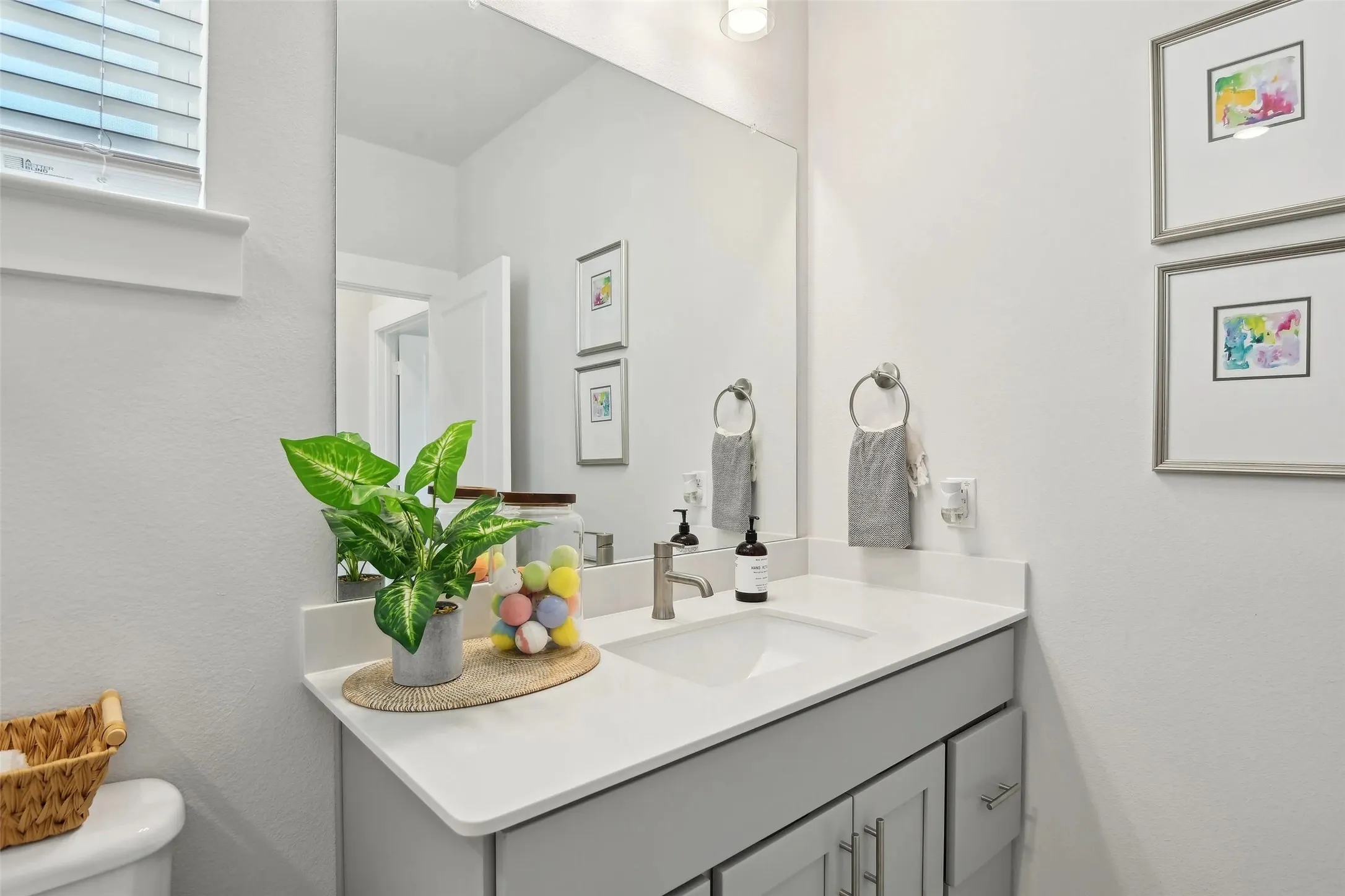 Recessed lighting illuminates a vanity with a white countertop and an integrated sink, complemented by a large wall-mounted mirror and light gray cabinetry